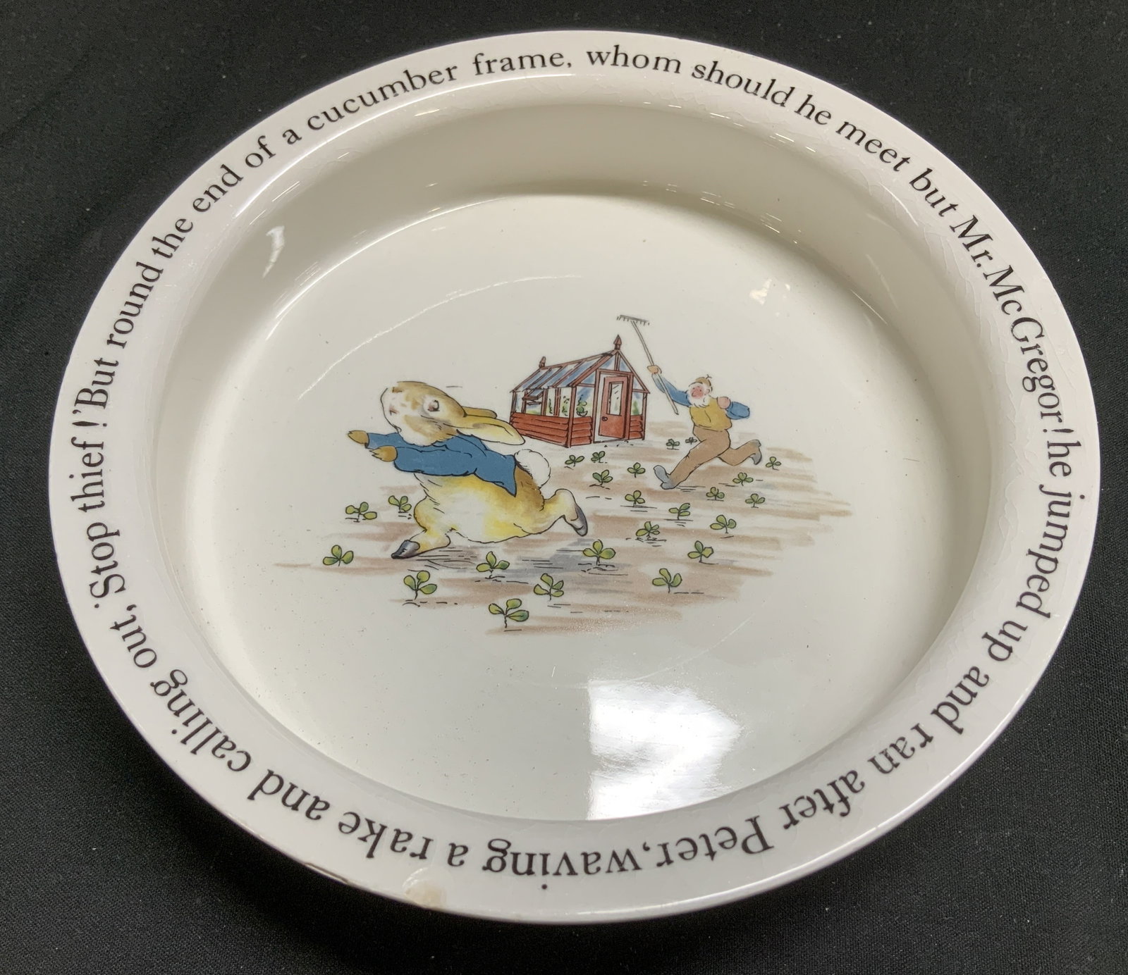 Wedgwood of Etruria Peter Rabbit Bwl ENGLAND: Wedgwood Peter Rabbit bowl features an illustration from Beatrix Potters classic tale, depicting Mr. McGregor chasing Peter Rabbit with a rake. Text around rim reads, But round the end of a cucumber f