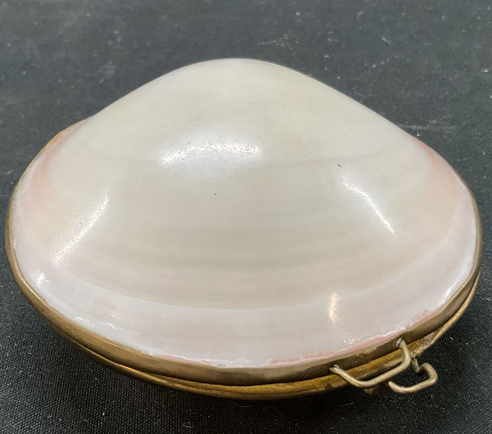 Vintage Hinged Clam Shell Trinket Box: Vintage hinged clam shell trinket box. Clam shell shaped. Brass toned accents and hinge. White color. Glossy finish. Measures approx 3.5 x 3.5 inches. Surface wear consistent with exposure. Trinket bo