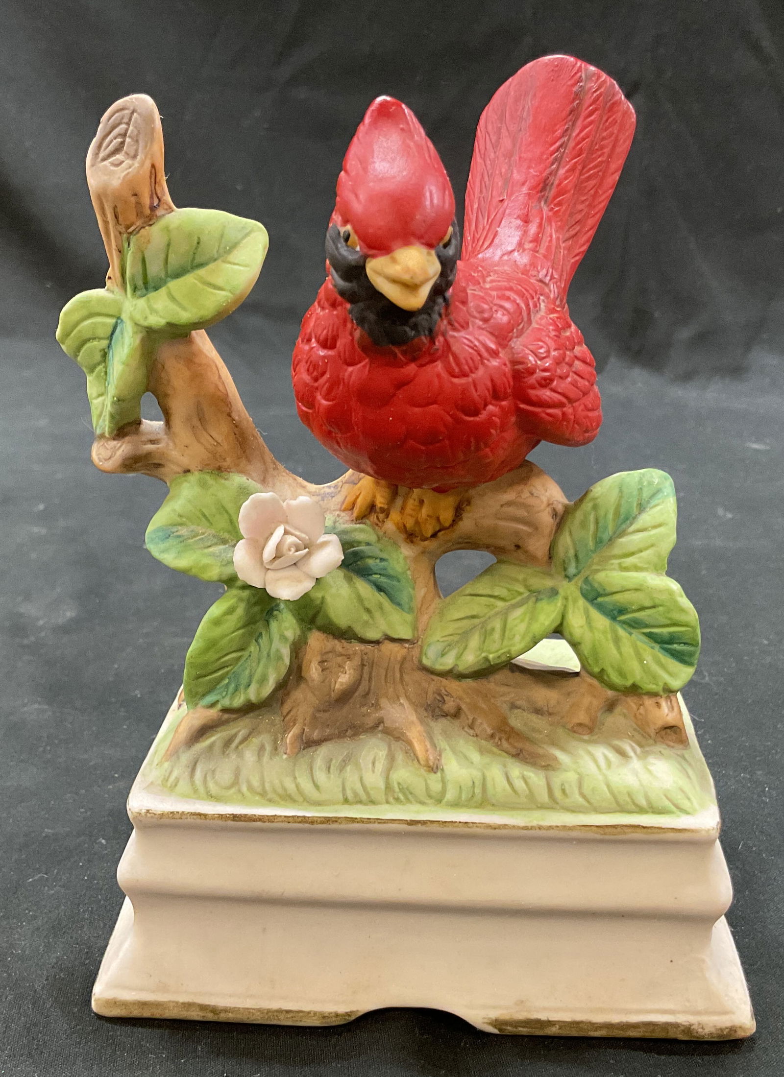Towle Porcelain Red Cardinal Music Box Korea: Towle porcelain red cardinal music box. Marked on underside, reads Towle Fine Porcelain Korea. Square pedestal base. Red cardinal bird perched on a flowering branch. Varying colors. Wind up music box.