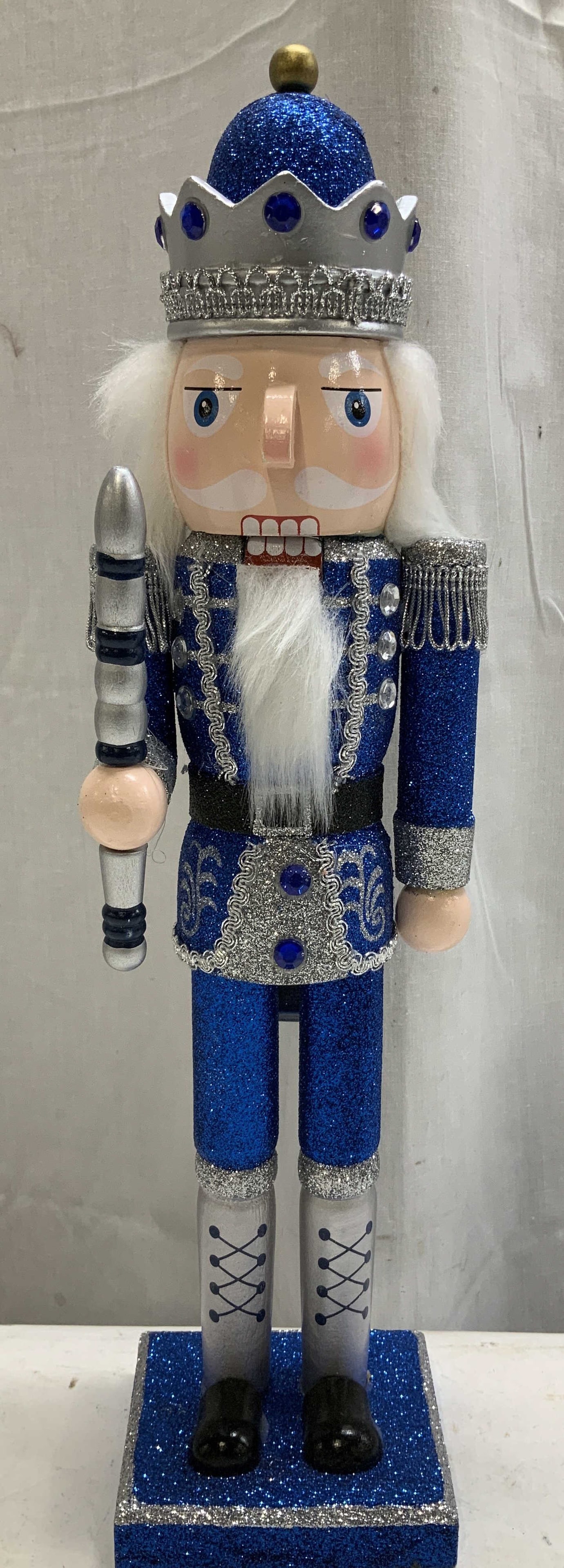 Signature Selects Wooden Nutcracker 15in: Signature Selects wooden nutcracker features a festive, glittering finish. Shades of blue & grey. Wearing crown. Signed & marked on underside. Reads, SIGNATURE SELECTS SEASONS. WOODEN NUTCRACKER. Surf