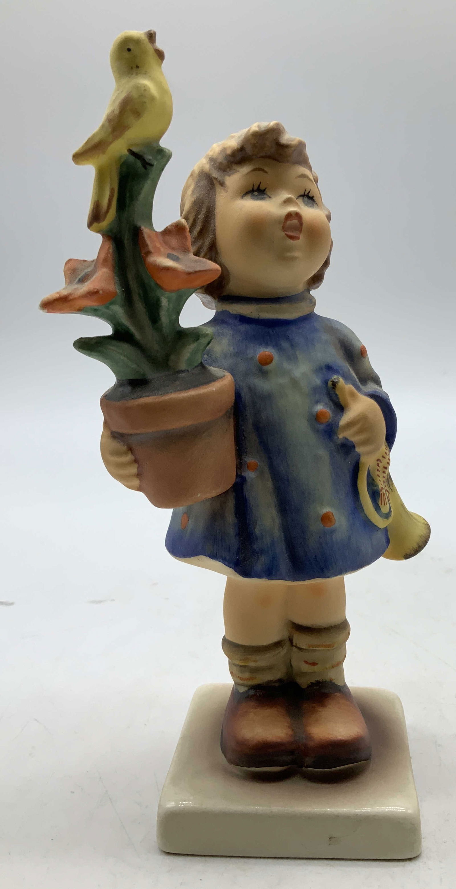 1971 Goebel Congratulations Ceramic Fig W GERMANY: 1971 Gobel ceramic figurine depicts a young girl in a blue dress holding a potted flower with a bird perched on top. Signed & marked on underside. Reads, GOEBEL W GERMANY. 1971. Surface wear consisten