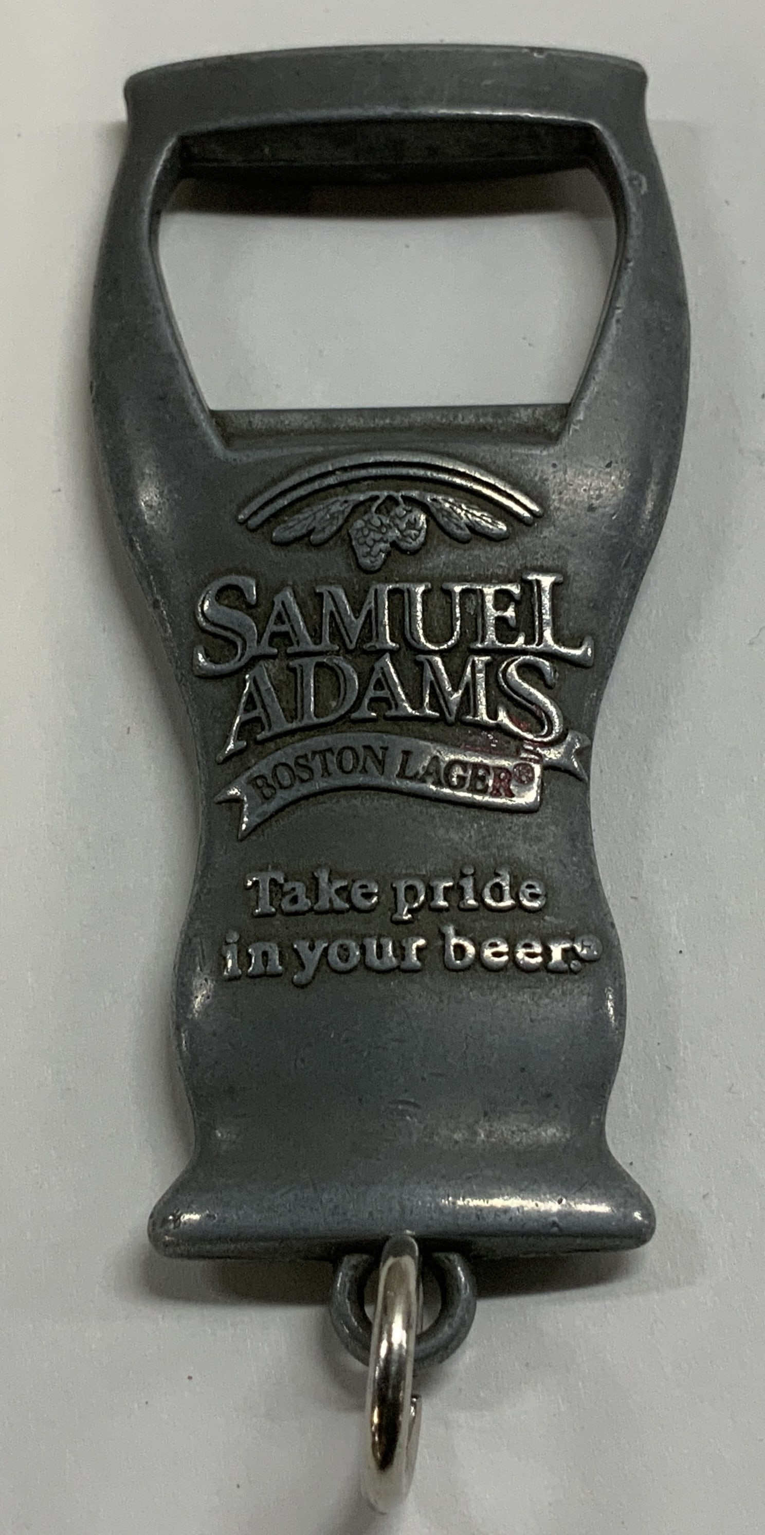 Samuel Adams Pewter Bottle Opener Keychain: Samuel Adams Boston Larger: Take pride in your beer. Pewter bottle opener keychain. Surface wear consistent to age, use & exposure. Measurements: length 2.6in x width 1.6in. Samuel Adams pewter bottle