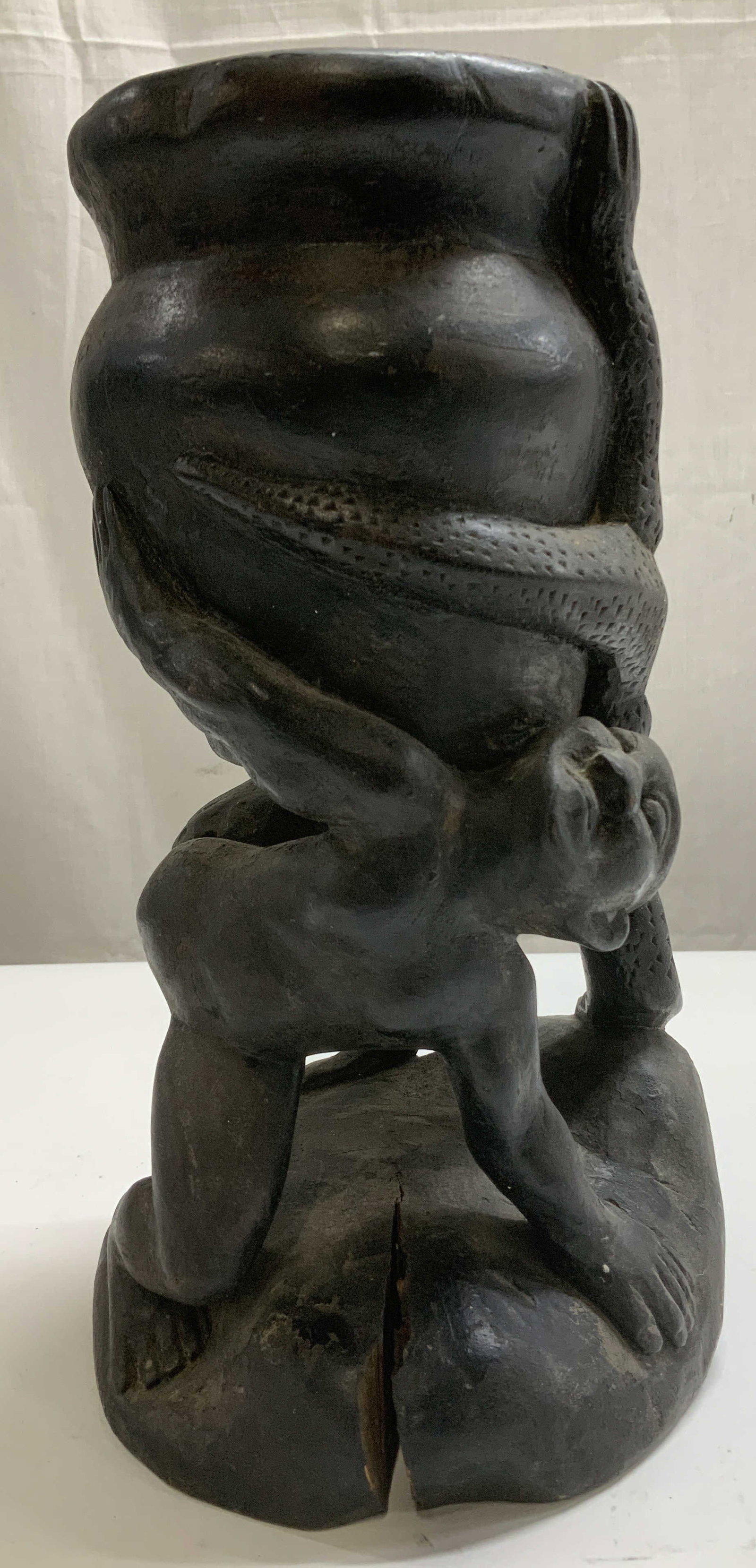 African Style Carved Wood Figural Vessel: African style carved wooden figural vessel featuring a design of a figure with one arm raised up & leg in reptiles mouth. Black toned. Opening at top. No visible signature or markings. Surface wear co