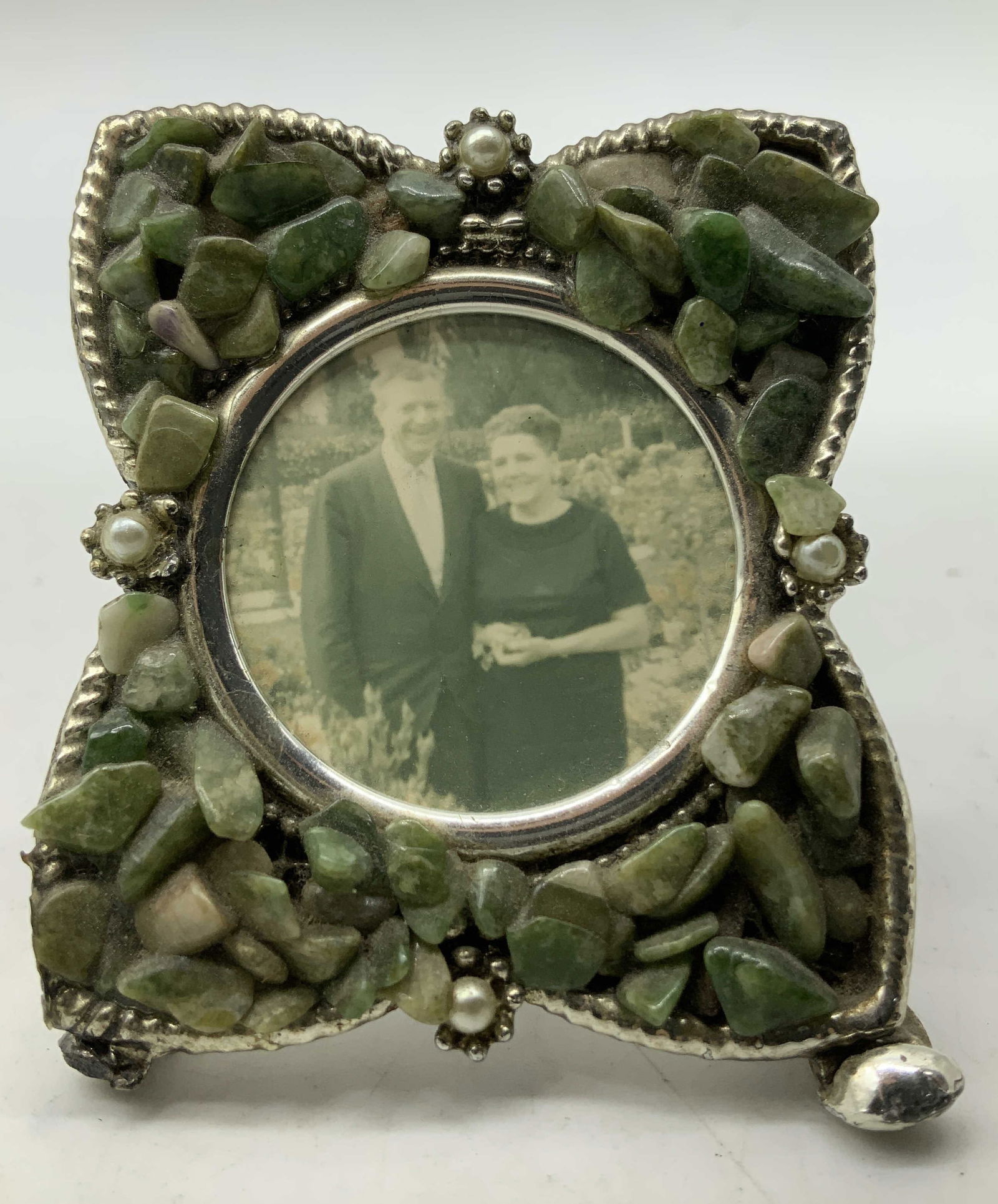 Vtg Silver Toned & Stone Picture Frame: Vintage frame features a silver toned finish & adorned with clustered green stones. 2 faux pearl at top & bottom. Center contains an image of a couple. No visible signature or markings, surface wear c