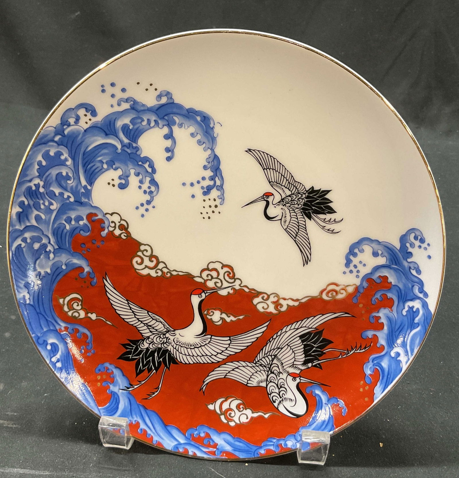 Takahashi Cranes & Waves Porcelain Plate: Takahashi cranes and waves porcelain plate. Signed on underside with Japanese characters. Gilt decorated rim. Circular plate. Three cranes flying over swirling blue and red waves, hand painted. Accent