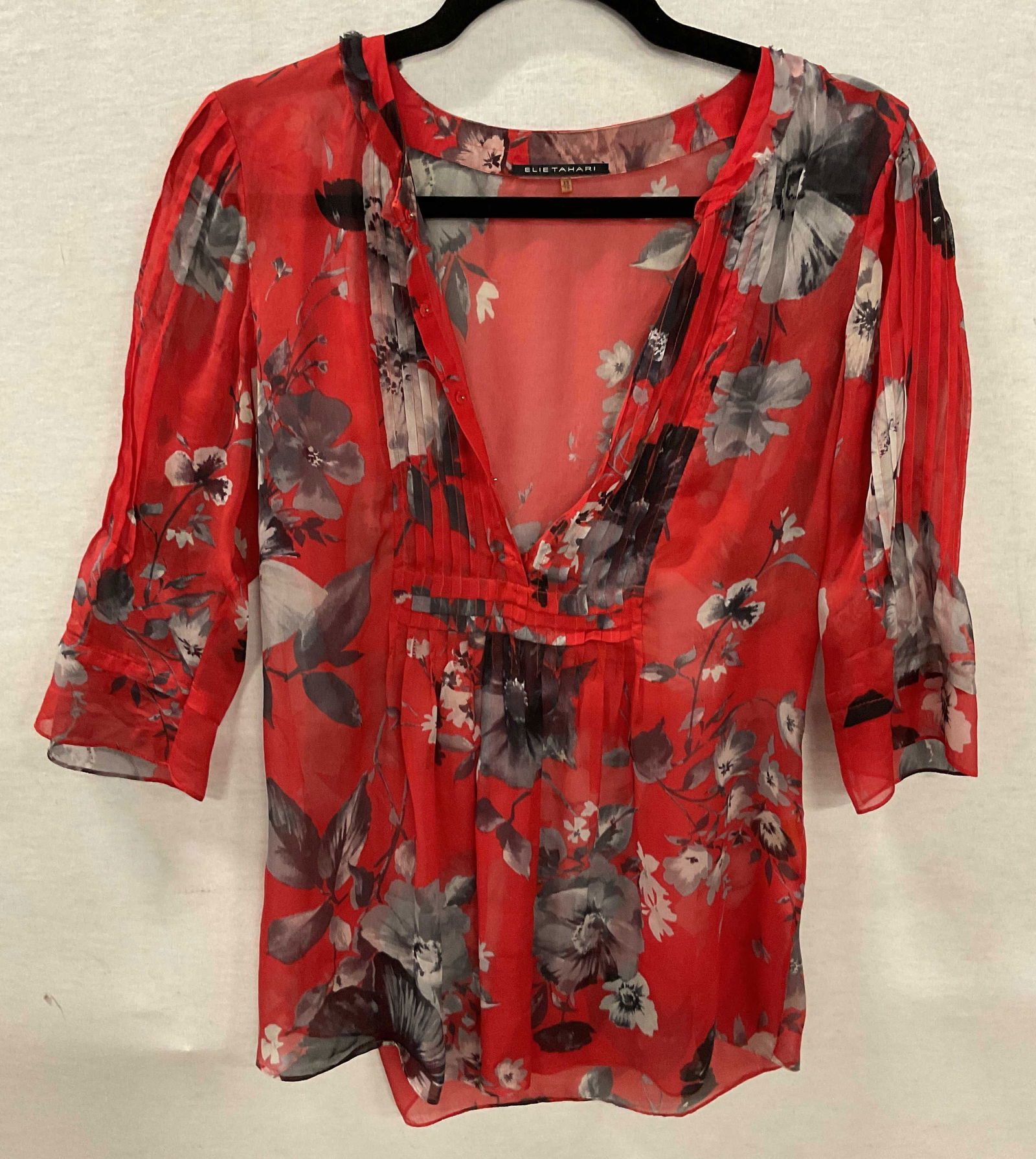 Elie Tahari Red Silk Sheer Floral Blouse: Elie Tahari red silk sheer floral blouse. Size XS. Silk material. Floral motifs in red, black, and white. Ribbed surface. Accented buttons. Ruffled collar. Flowed sleeves. Wear consistent with exposur