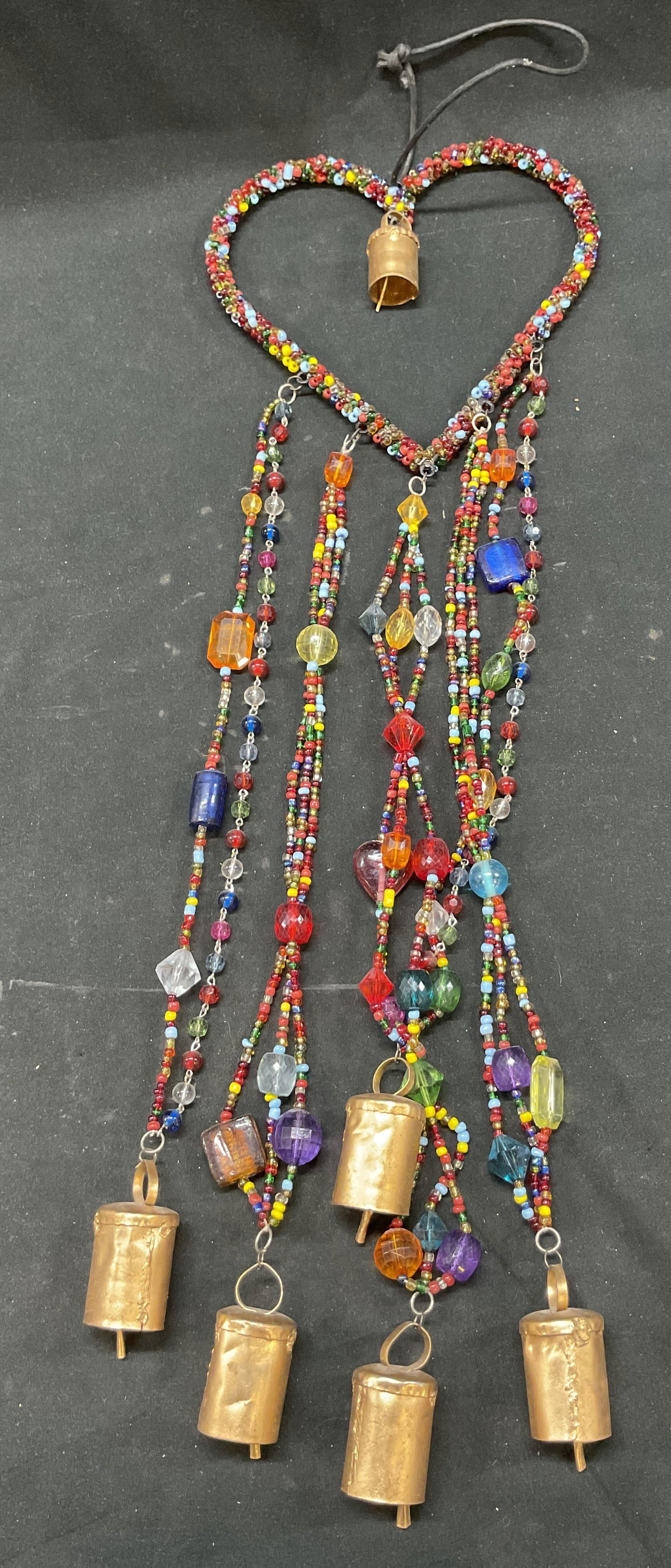 Vintage Beaded Heart Bell Wind Chime: Vintage beaded heart bell wind chime. Heart shape made of beads. Long beads hang down. Vary in shape and size. Brass toned bells. Varying colors. String attached. Measures approx 4 x 21 inches. Surfac