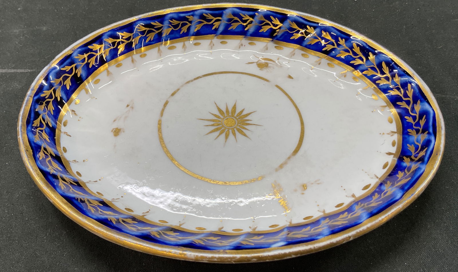 Vintage Porcelain Hand Painted Trinket Dish: Vintage porcelain hand painted trinket dish. Oval shaped. No visible markings. Ribbed surface. Hand painted blue and gilt floral and sun motifs. Measures approx 6 inches in diameter. Surface wear cons