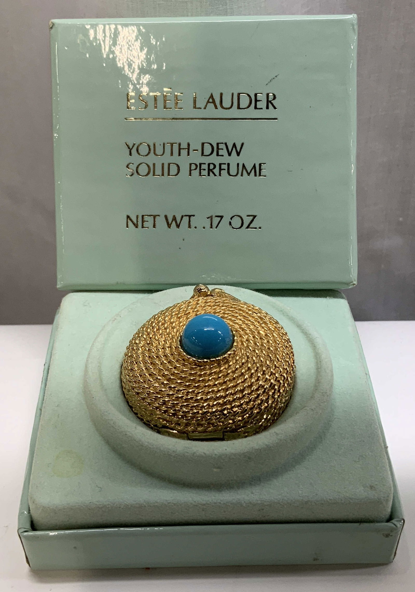 C.1960s Estee Lauder Solid Perfume Compact W Bx: C.1960s Estee Lauder solid perfume compact features a coiled rope style design. Gold toned & faux turquoise stone in center. Comes with fitted box. Sold as is. Surface wear consistent to age, use & ex