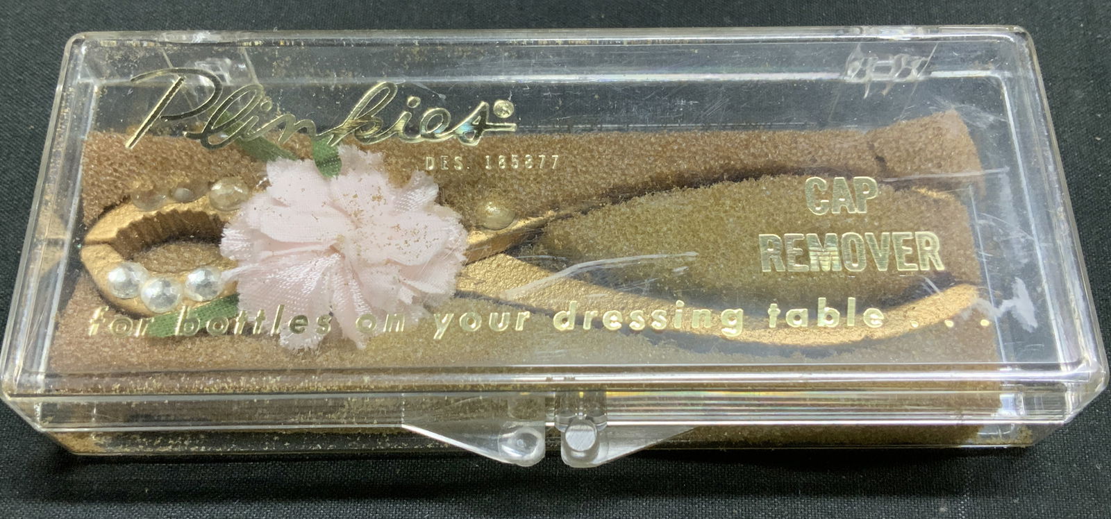 Vtg Plinkies Dresser Cap Remover W Org Box: Vintage Plinkies cap remover designed to help open bottles on a dressing table. Cap remover is embellished with rhinestones & a pink floral accent. Gilt toned. Comes with original box. Surface