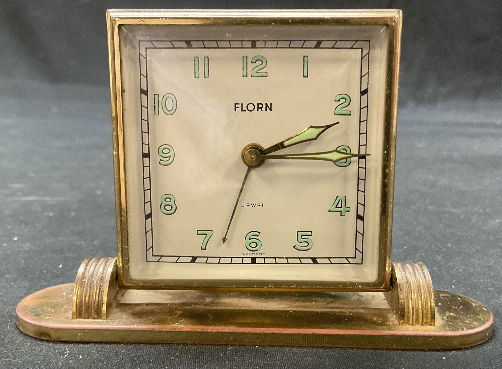 Vtg Florn 8 Day Art Deco Desk Clock Germany: Vintage Florn 8 day Art Deco brass toned desk clock. Face is marked Florn Jewel Germany. The backside is marked The Florn Comp Germany US Zone. Oval base with slopes. Clock moves back and forth. Squar