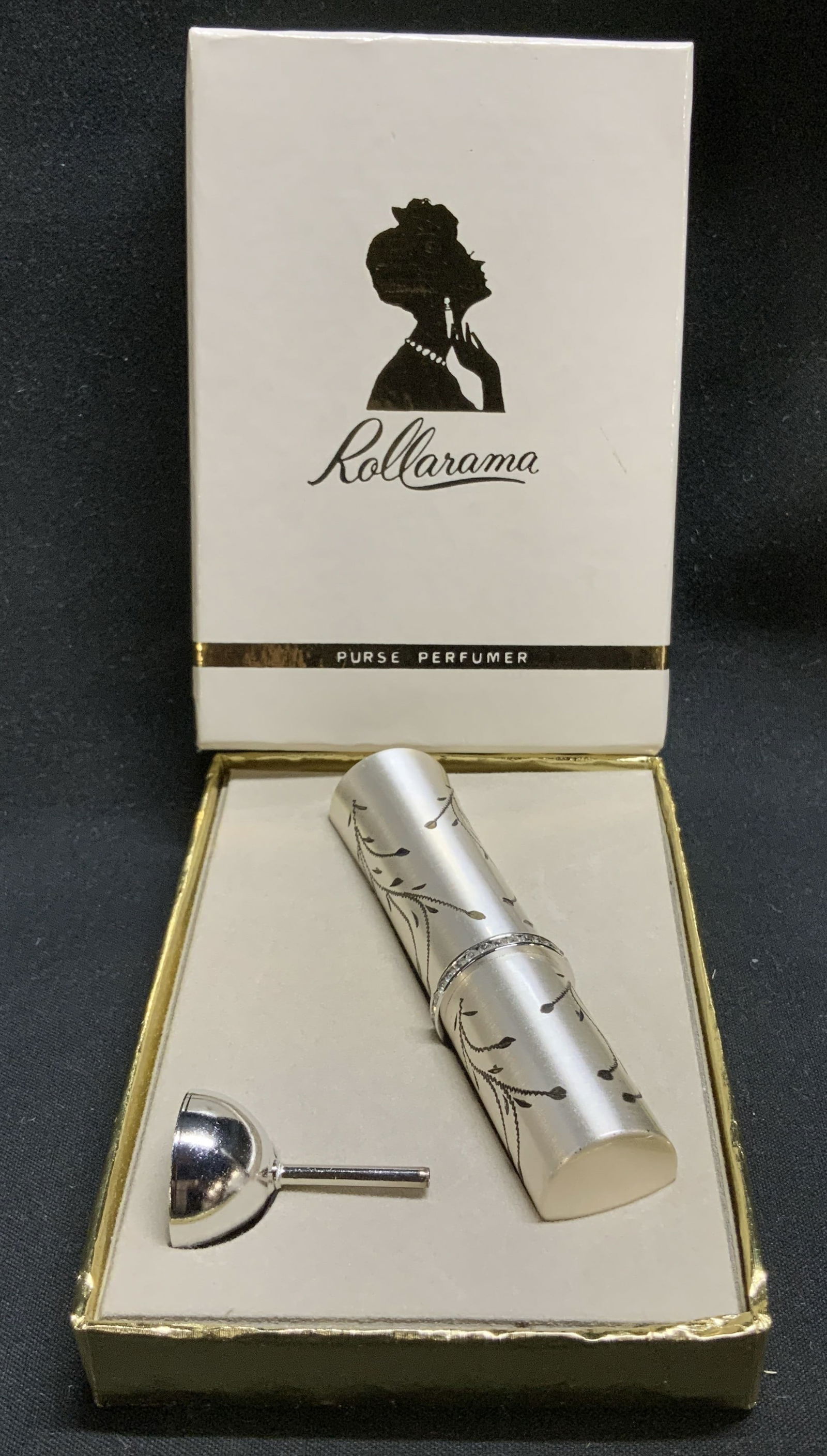 Vtg Lyric Rollarama Purse Perfume W Org Box: Vintage Lyric rollarama purse perfume features a silver toned finish with floral accents. Rhinestone detailing. Comes with original box. Sold as is. Signed & marked. Reads, ROLLARAMA. PURSE