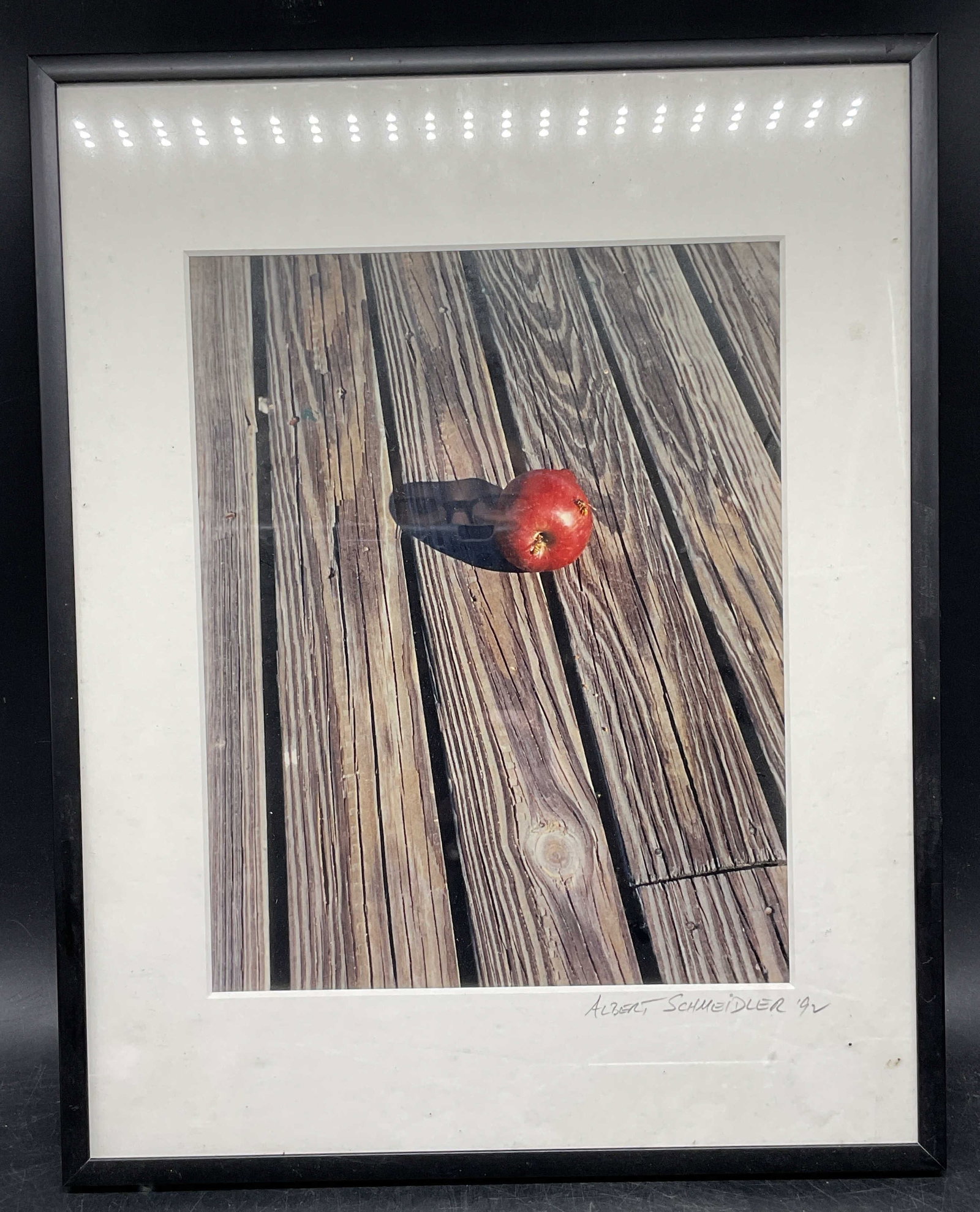 Signed Schmeidler Apple & Bee Photograph 24.5in: Framed and matted photograph. Signed on the mat, Albert Schmeidler. Apple with bees. Black frame. Not examined out of frame. Frame measures approx. 24.25 x 11.25 inches. Some wear consistent with expo