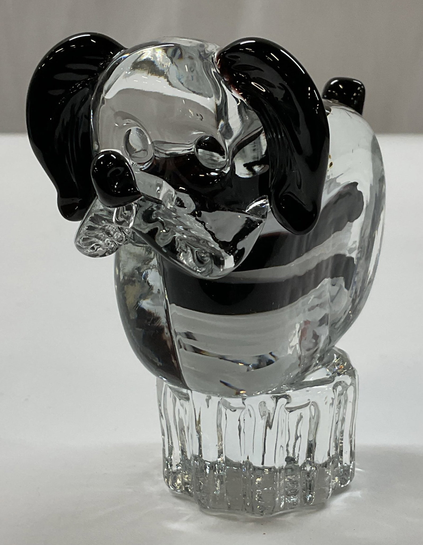 Hand Blown Art Glass Dog Figurine: Hand blown art glass dog figure. Clear glass body with swirled black and white accents. Dog sits on a ribbed scalloped base. No visible markings. Detailed features and textures. Measures approx 2.5 x