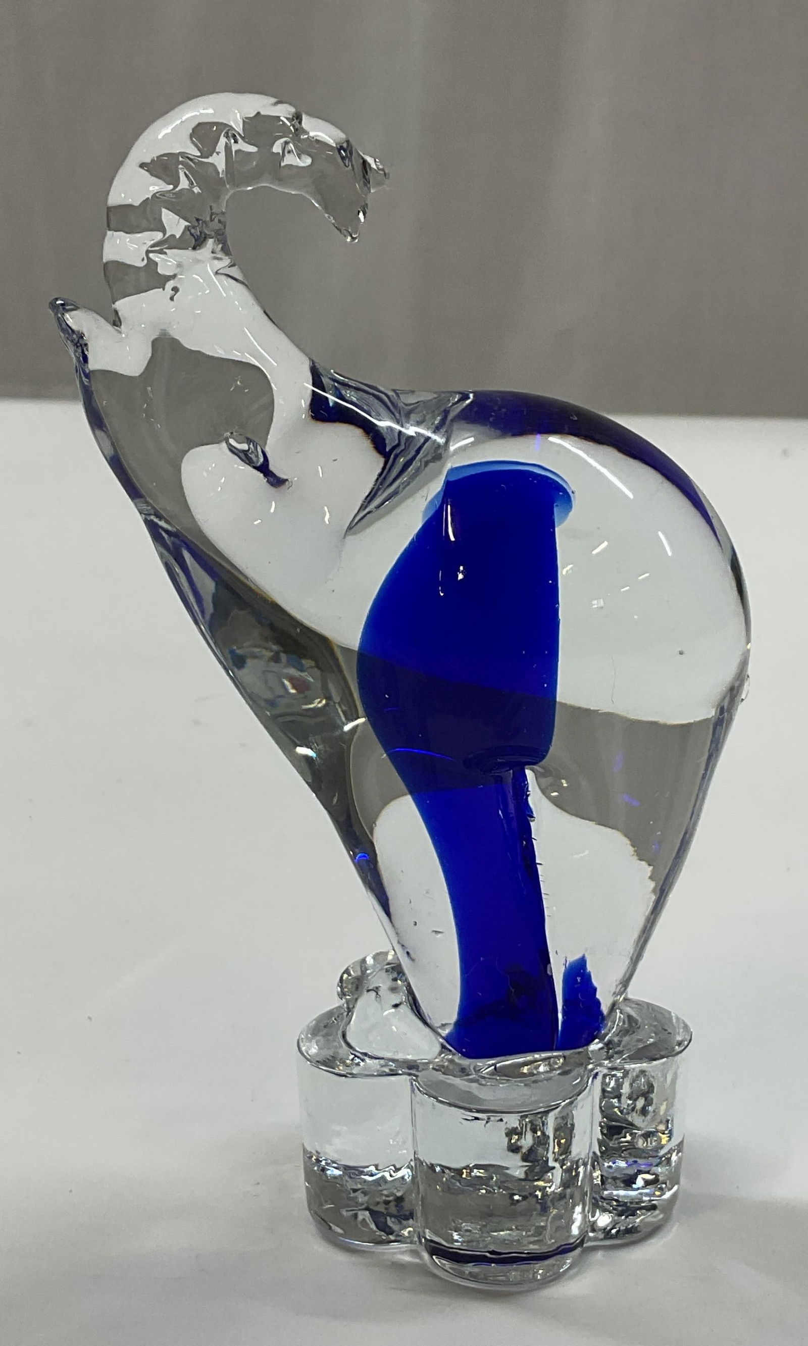 Hand Blown Art Glass Elephant Figure: Hand blown art glass elephant figure. Clear glass body with blue swirled design. Elephant sits on a ribbed scalloped base. No visible markings. Detailed features and textures. Measures approx 2 x 4 x