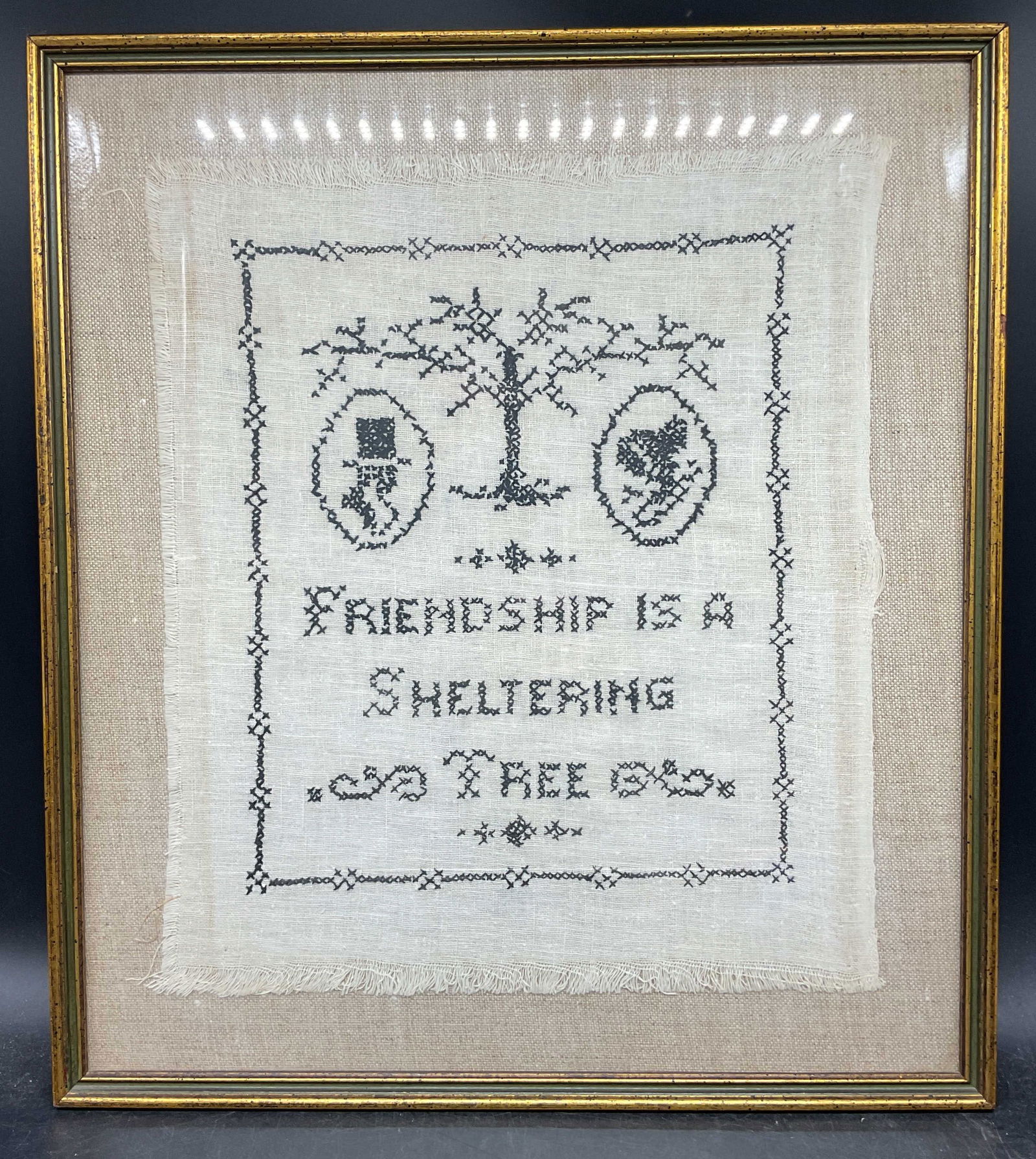 Framed Friendship Cross Stitch Sampler: Framed and mounted cross stitch sampler. Black thread on white linen. Friendship is a sheltering tree. Tree and figural motifs. Gilt wood frame. Not examined out of frame. Frame measures approx.