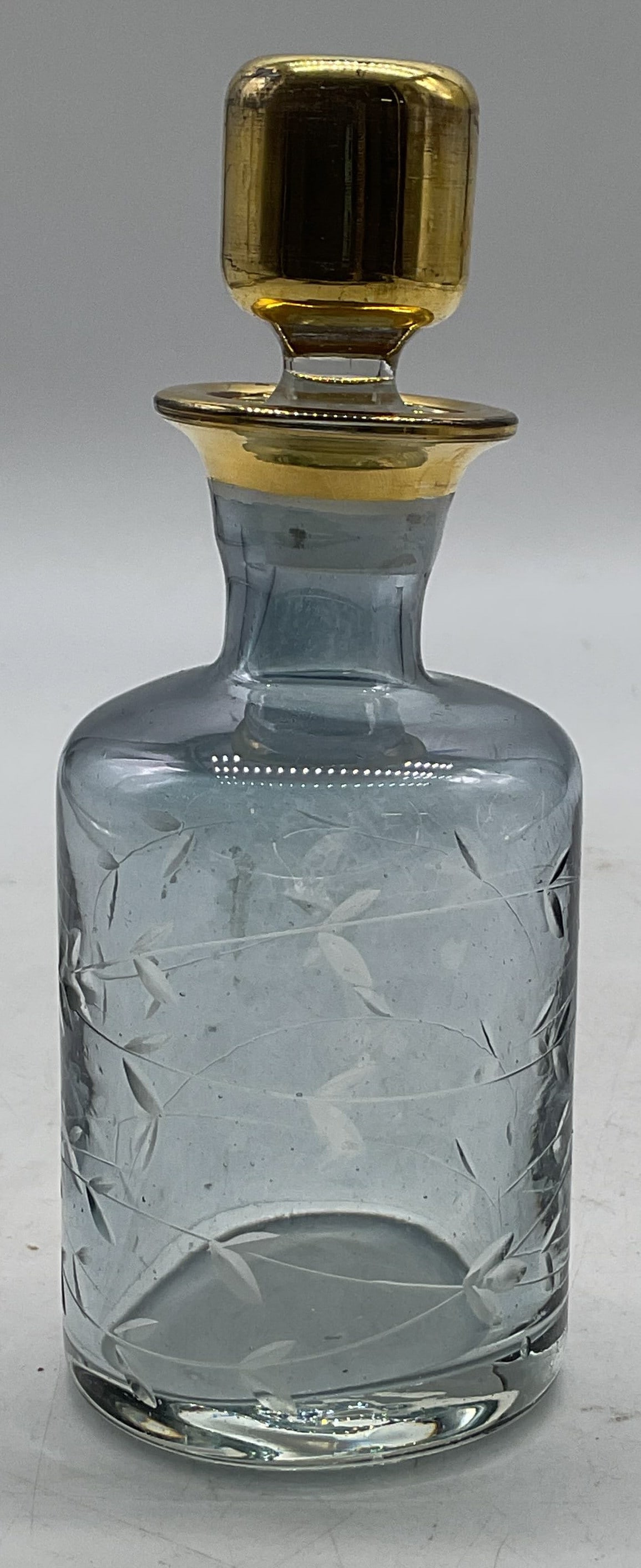 Vintage Etched Glass Perfume Decanter W Stopper: Vintage etched glass perfume decanter. Gold toned stopper and rim. Blue tinted glass. Etched leaf motifs. Round base. Measures ht approx 6 inches base diam approx 2.5 inches. Surface wear
