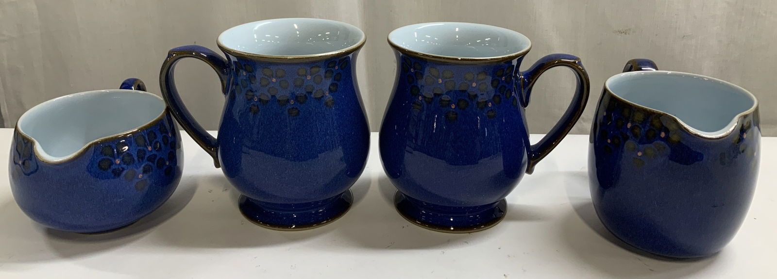 Set 4 Denby Midnight Cups & Creamers ENGLAND: Lot includes, 2 cups & 2 creamers. Pieces features a blue glaze with a brown spotted design. Midnight pattern. Appears to be possible stoneware material. Signed & marked on underside. Reads, DENBY ENG