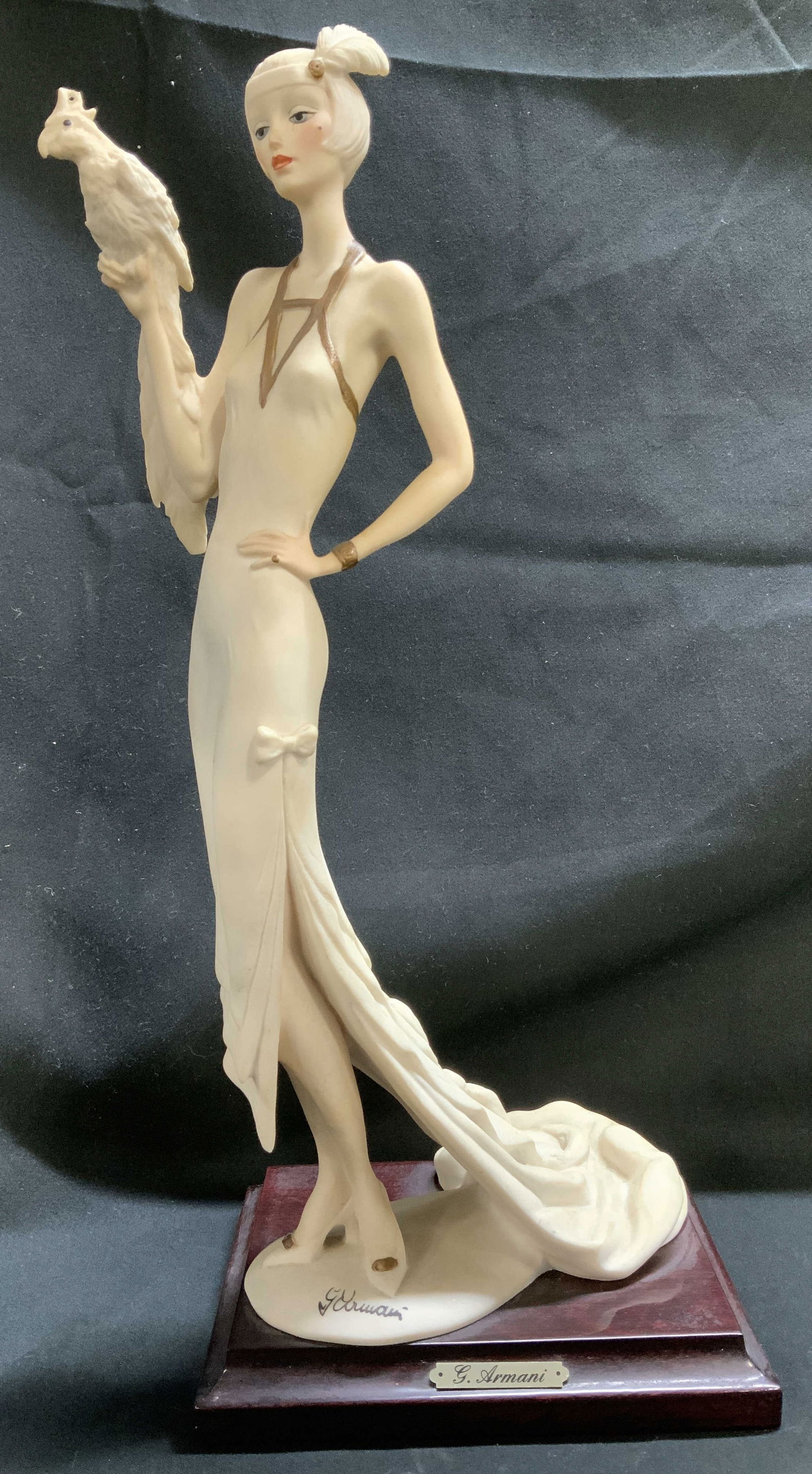 1987 Sgnd Giuseppe Armani Lady W Parrot Fig ITALY: 1987 Giuseppe Armani figurine depicting a woman in a long white gown holding a bird. Gilt accents on her dress. Figurine is mounted on a dark wooden base with a gold toned plaque. Reads, G. Armani. Si