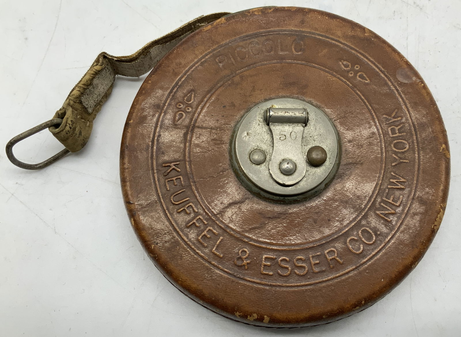 Vtg Keuffel & Esser Co. Piccolo Tape Measure NY: Vintage Keuffel & Esser Co. New York Piccolo tape measure, featuring a distinctive circular brown leather case. Surface wear consistent to age, use & exposure. Sold as is. Measurements: length 3.8in x