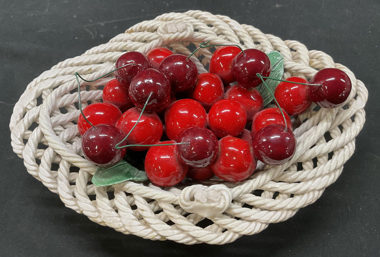 Vintage Ceramic Cherry Basket Sculpture Italy: Vintage ceramic cherry basket sculpture. Marked on underside, reads illegibly, made in Italy. White oval basket with basket weave appearance. Ribbed surface. Red cherries and green leaves sit in baske