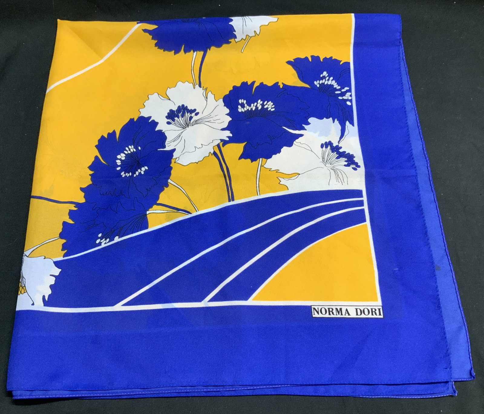 Norma Dori Blue & Yellow Square Scarf ITALY: 100% polyester. Made in Italy. Scarf features floral motifs. Shades of blue, yellow & white. Square shape. Signed & marked. Reads, NORMA DORI. Surface wear consistent to age, use & exposure. Measureme
