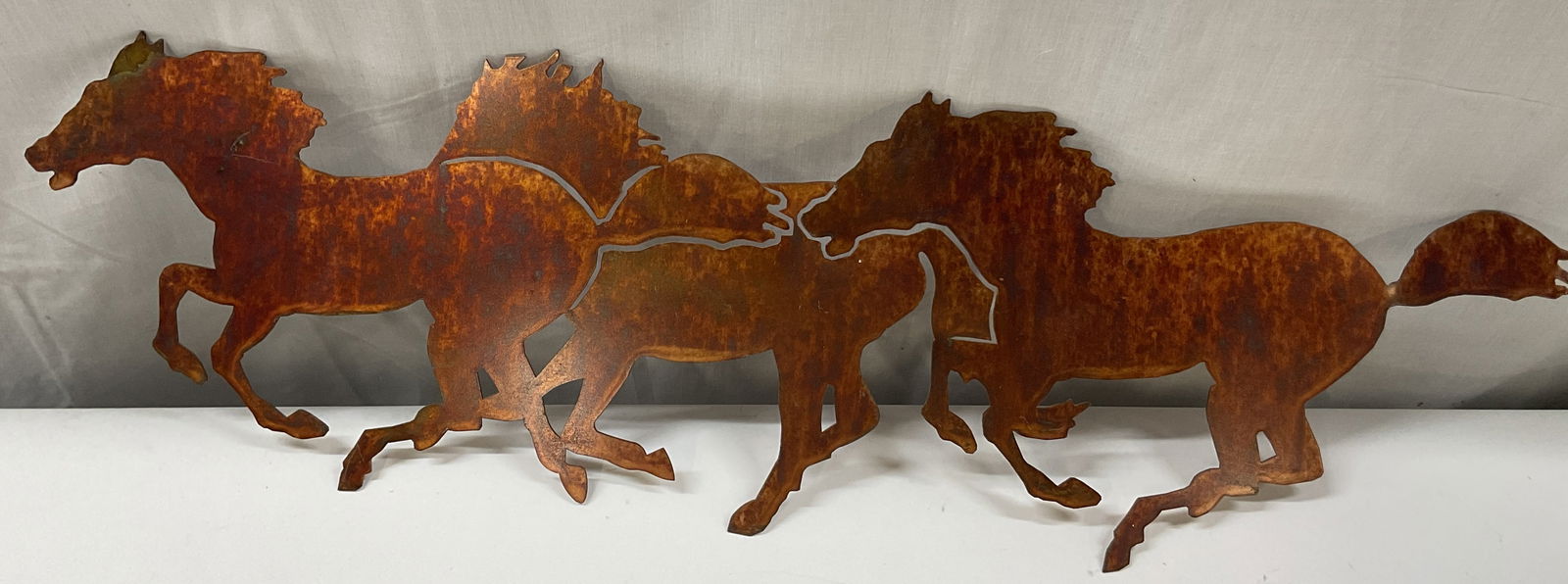 Vtg Metal Rustic Galloping Horses Wall Art 2ft: Vintage metal rustic toned galloping horses wall art. Rustic toned appearance. Trio of silhouetted galloping horses. Measures approx 6 x 24 inches. Surface wear consistent with exposure, scratching. W