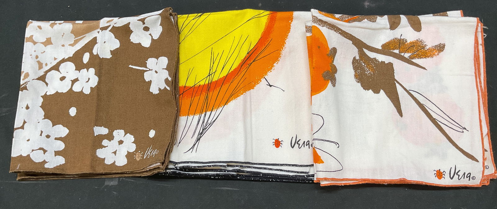Lot 10 Vera Neumann Decorative Cotton Napkins: Lot of 10 Vera Neumann decorative cotton napkins. Cotton material. Signed. Colors consist of brown, white, orange, yellow, and more. Features floral, butterfly, fruit, and sun motifs. Measures