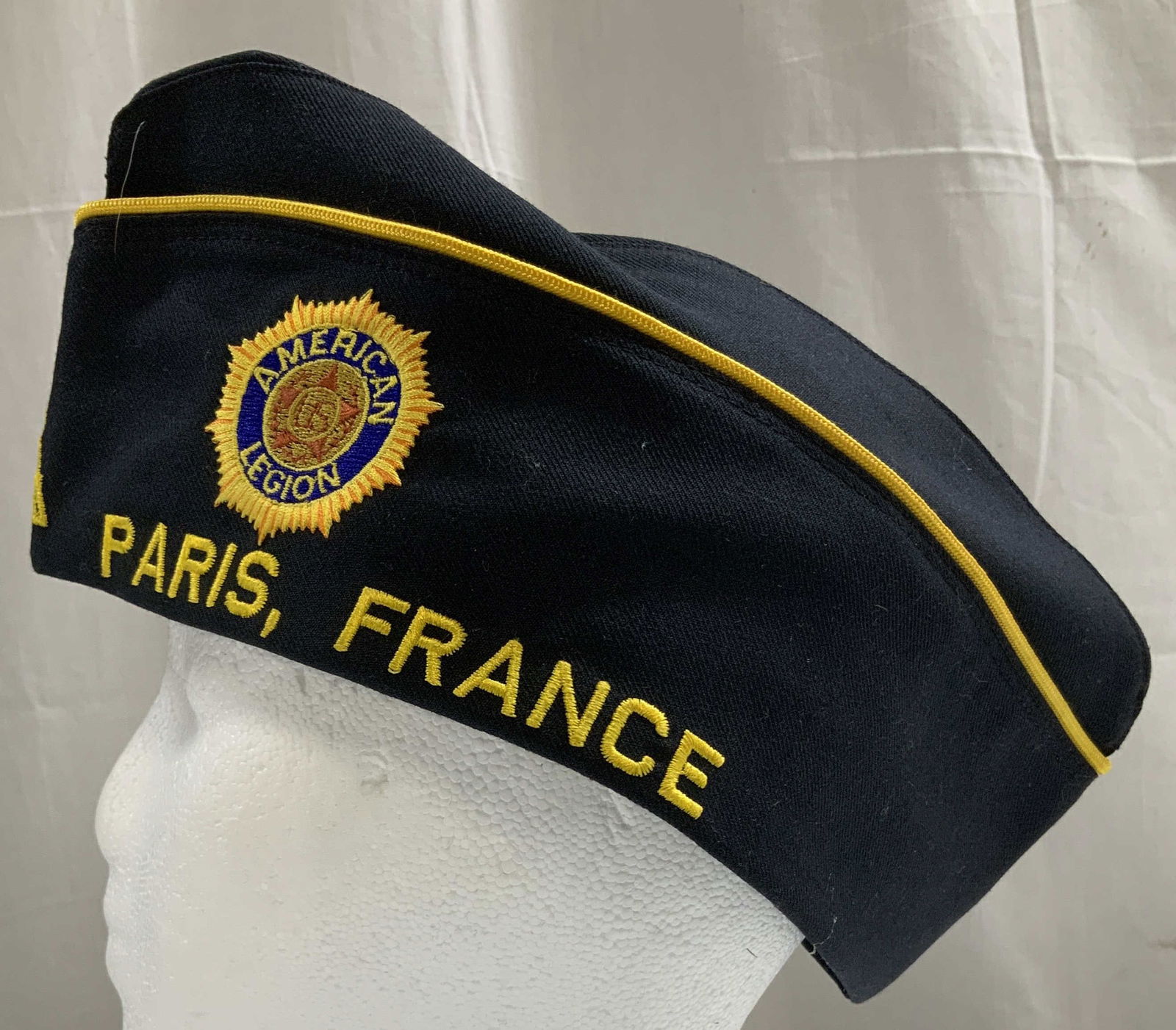 Vtg American Legion Paris, France Garrison Cap: Vintage garrison cap is dark & yellow toned. Circular embroidered emblem with AMERICAN LEGION. Yellow capital words read, Paris, France. Embroidered Eiffel tower. Dacron wool. Size 7 3/8. Signed & mar