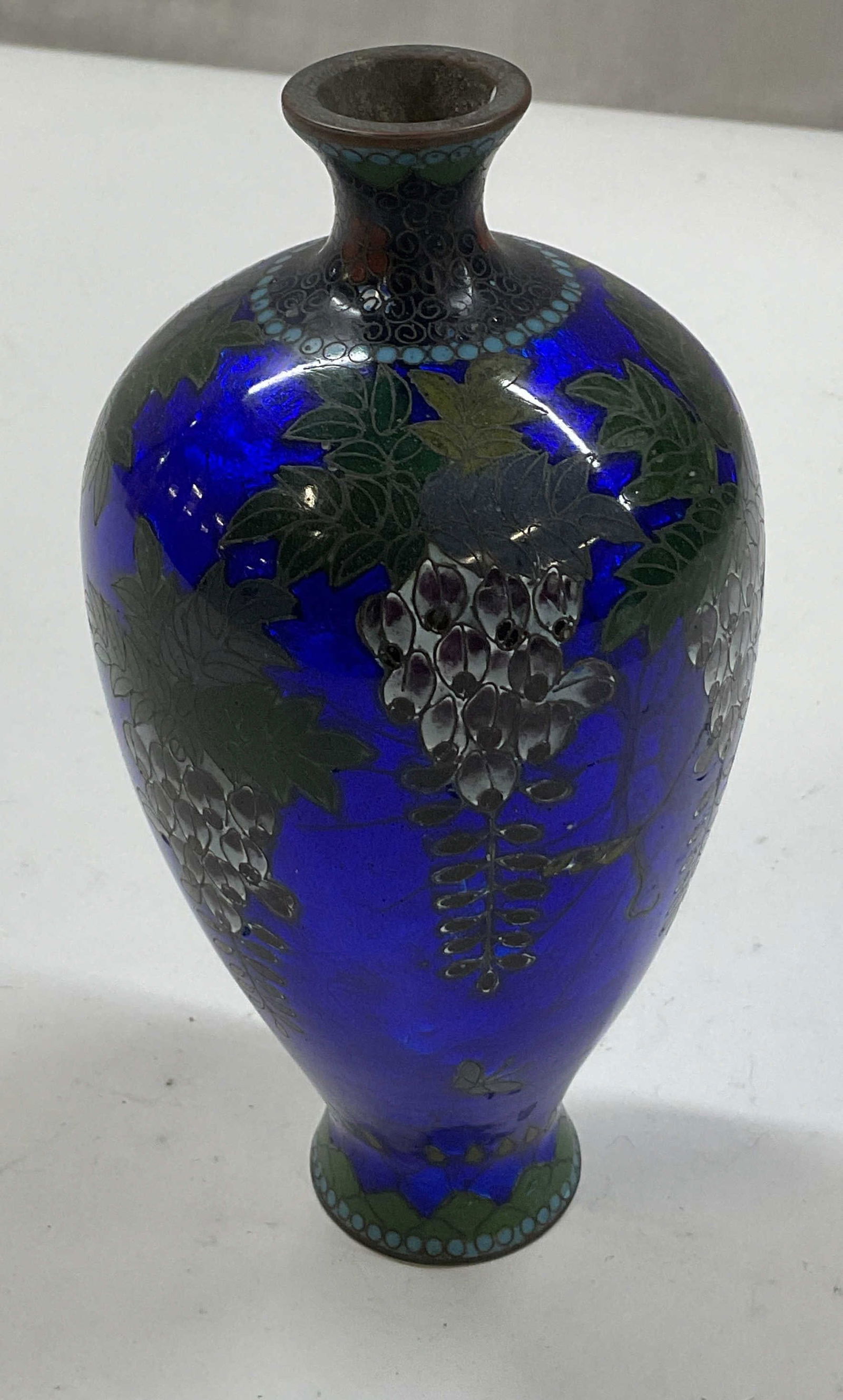 Vintage Enameled Brass Cobalt Blue Bud Vase: Vintage enameled brass cobalt blue bud vase. Chinese cloisonne style. Round bulbous body and flat vase. Tiny flared rim. Hand painted fruit, floral, and butterfly motifs in varying colors. Shiny cobal