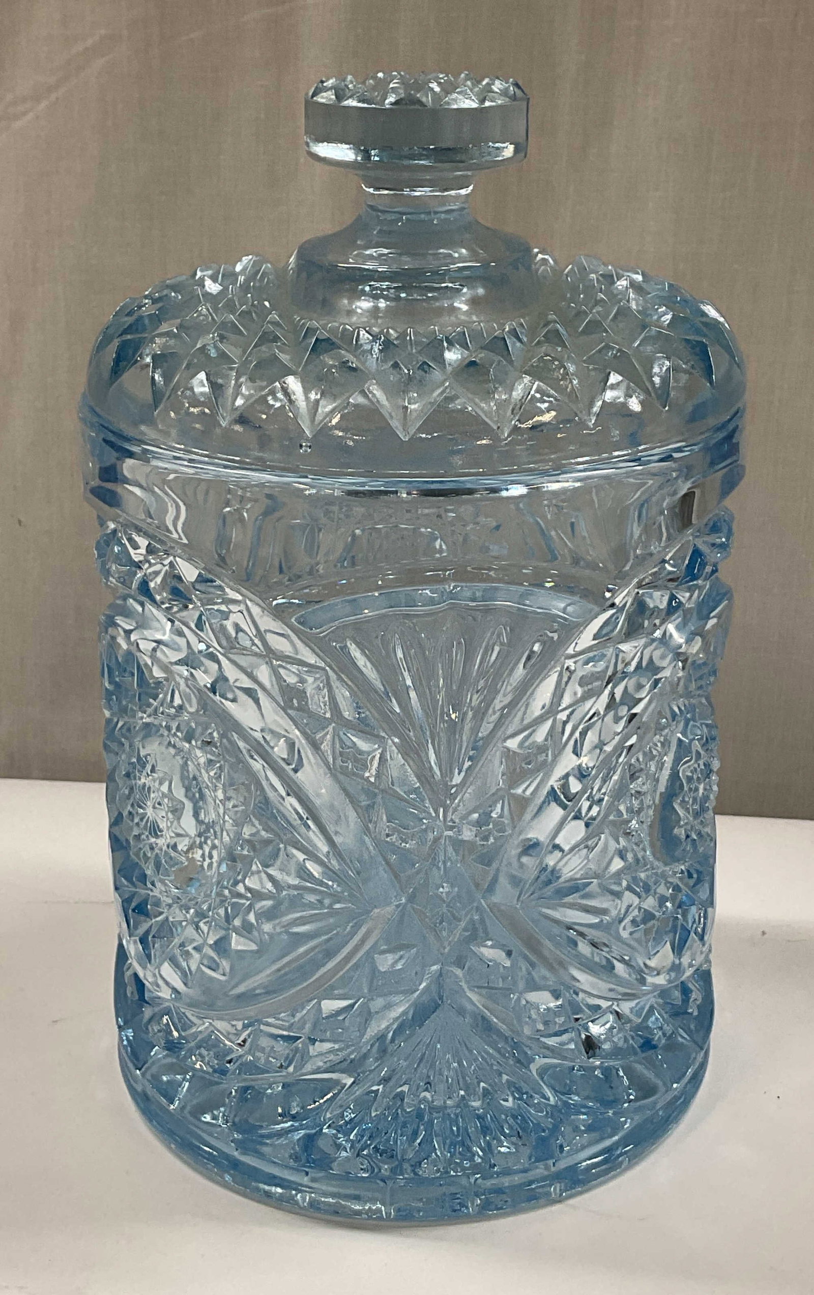 Imperial Glass Blue Hobstar Glass Biscuit Jar: Imperial Glass blue hobstar glass biscuit jar with lid. Cylindrical shape. Cut hobstar pattern. Star and fan patterns. Decorative finial on lid. Measures ht approx 8.5 inches diam approx 6 inches. Som