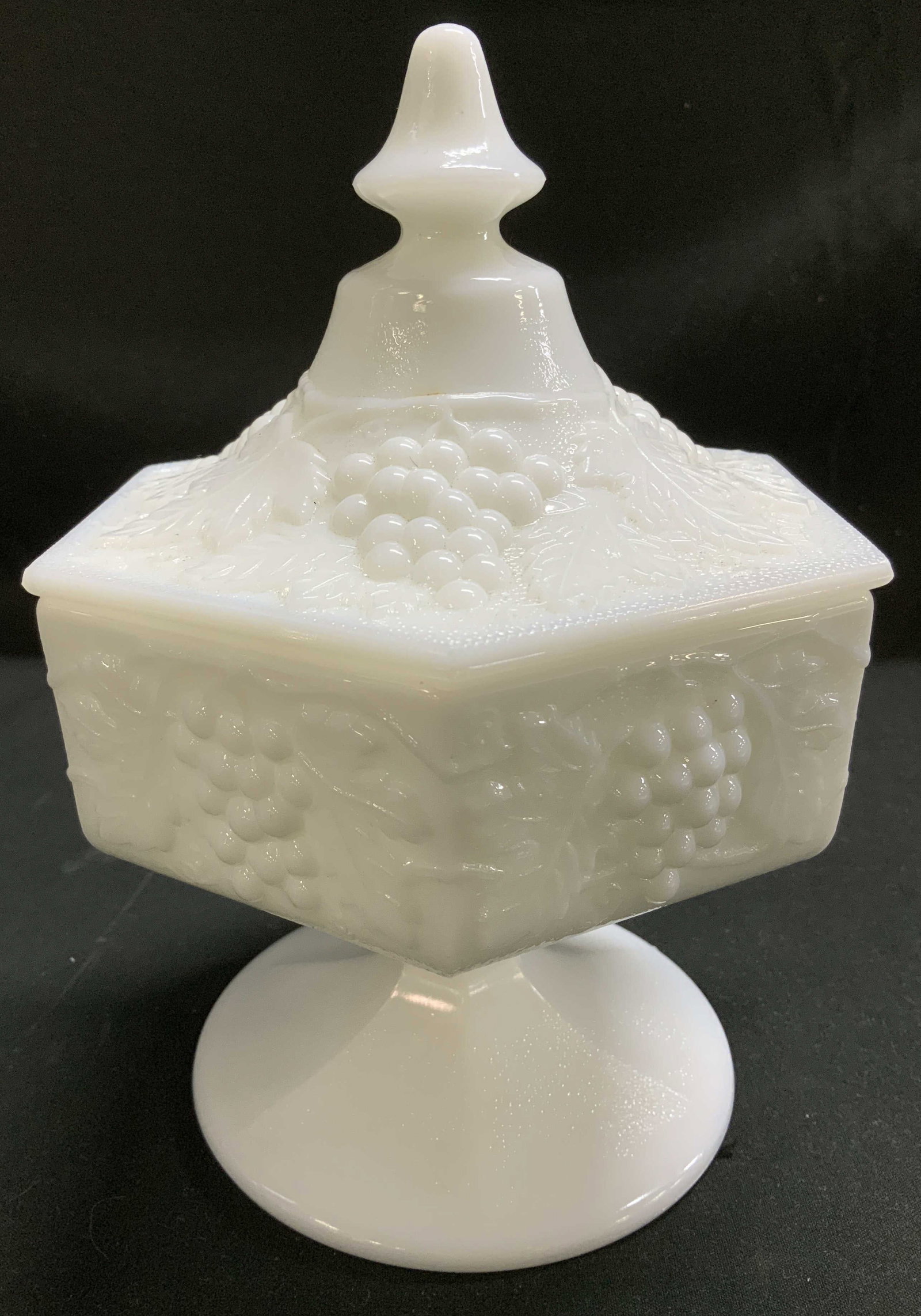 Vtg Imperial Milk Glass Lidded Candy Dish: Vintage Imperial milk glass candy dish features an embossed grape & leaf design. Pedestal base & hexagonal lid with finial. Signed & marked on underside. Surface wear consistent to age, use & exposure