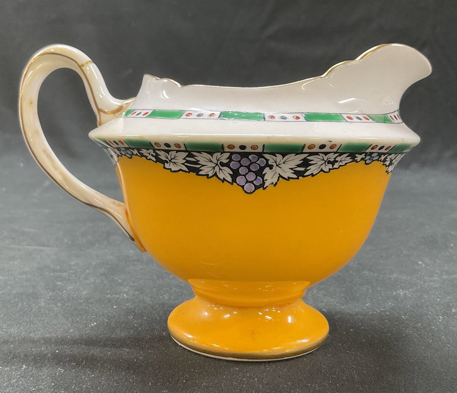 Shelley Bone China Creamer England: Shelley bone china creamer. Marked on underside, reads Shelley China England. Curved twisted design handle and spout. Scalloped edge. Gilt decorated rims. Pedestal base. Yellow background with hand pa