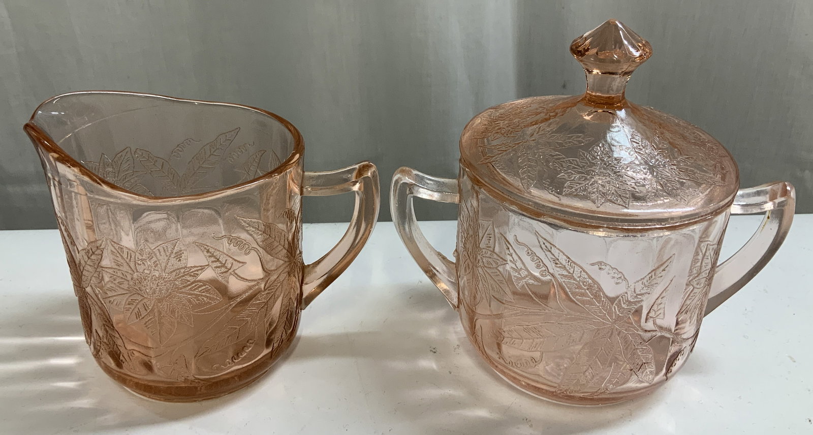 Vtg Pink Depression Glass Creamer & Sugar Bwl Set: Vintage pink depression glass creamer & lidded sugar bowl set. Features an embossed poinsettia design. Surface wear consistent to age, use & exposure. No visible signature or markings. Surface wear co