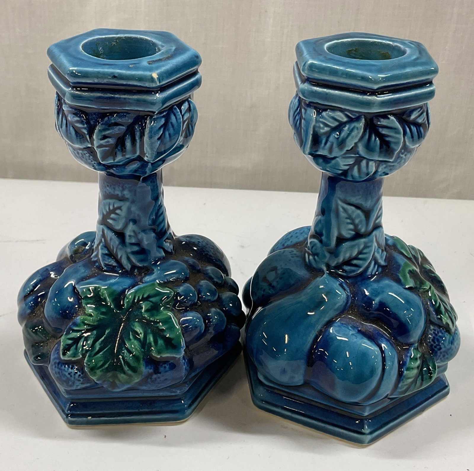 Pair Inarco Indigo Blue Candle Holders Japan: Pair of Inarco mood indigo blue ceramic candle holders. Marked on underside, reads Inarco Japan. Embossed fruit and leaf motifs. Curved edge base. Blue with green accents. Glossy finish. Measures ht a