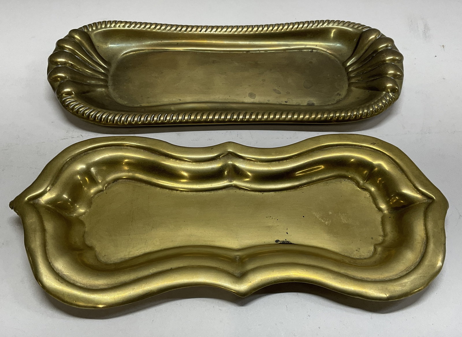 Lt 2 ATQ British Brass Trays: Lot of 2 Antique British Brass Trays. Decorative borders. Some discoloration consistent with age. Chip on edge of smaller. Largest measures app 9.5in H x 4in W. home decor, home accessories, table dec