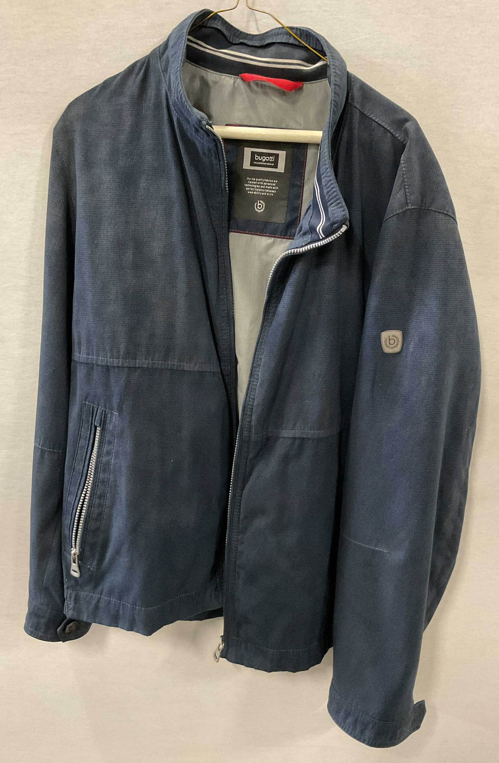 Bugatti Blue Zippered Jacket Germany: Bugatti blue zippered jacket. Designed in Germany. Size 46R. Nylon material. Blue exterior with grey interior and red accents. Collared. Front zipper and pockets. Wear consistent with exposure. Jacket