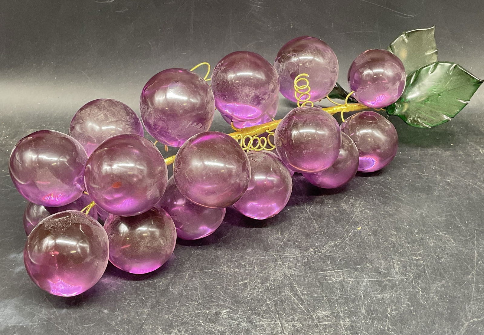 Art Glass Purple Grape Cluster Figurine: Hand blown art glass grape cluster figurine in purple and green. Gold metallic thread wrapped wire. Measures approx. 14 inches long, 3 inches wide. Some scratching. Art glass grade, grape figurine, co