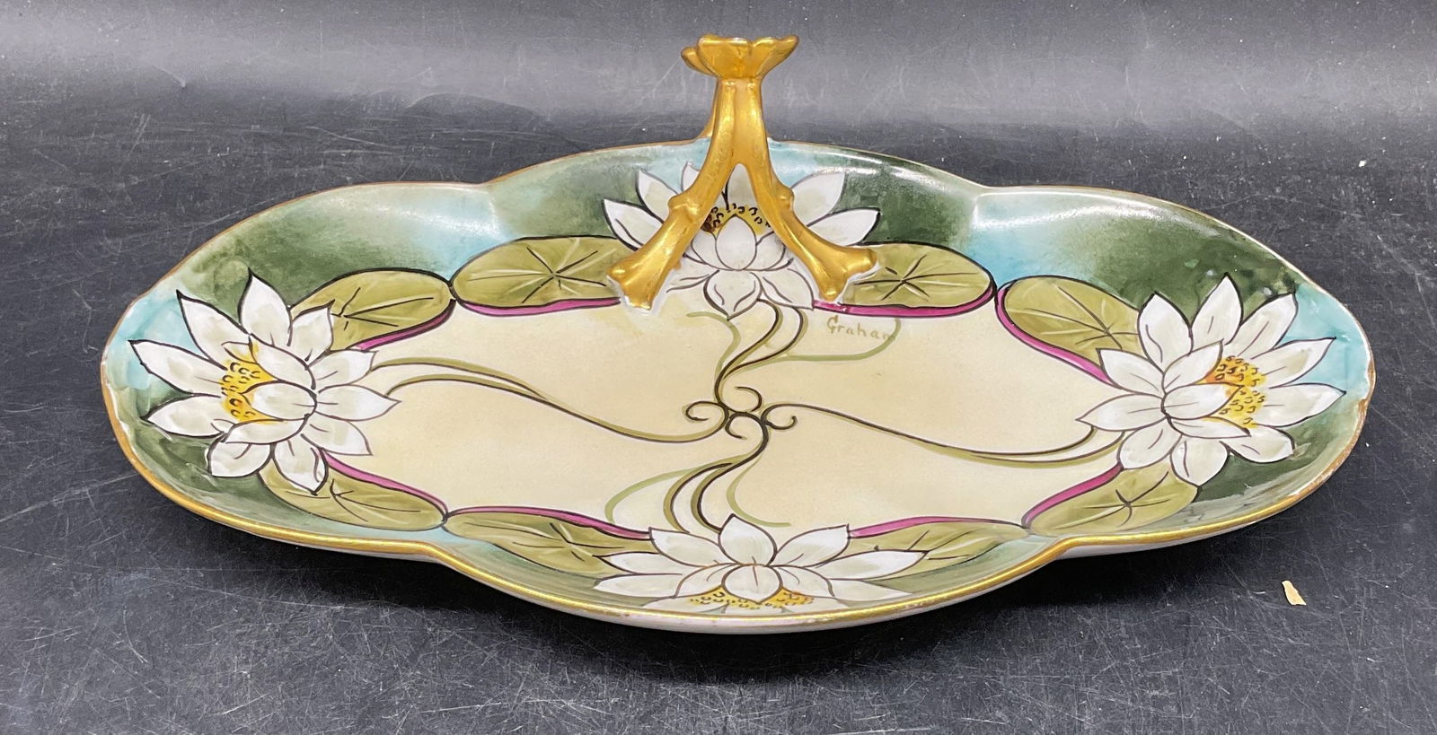 Guerin Limoges Porcelain Lily Platter, France: Antique William Guerin & Co Limoges porcelain platter with handle. Signed W. G. & Co. Hand painted water lily motif, signed Graham on the plate. Gilt handle. Measures approx. 10.75 x 6.75 x 3 inches.