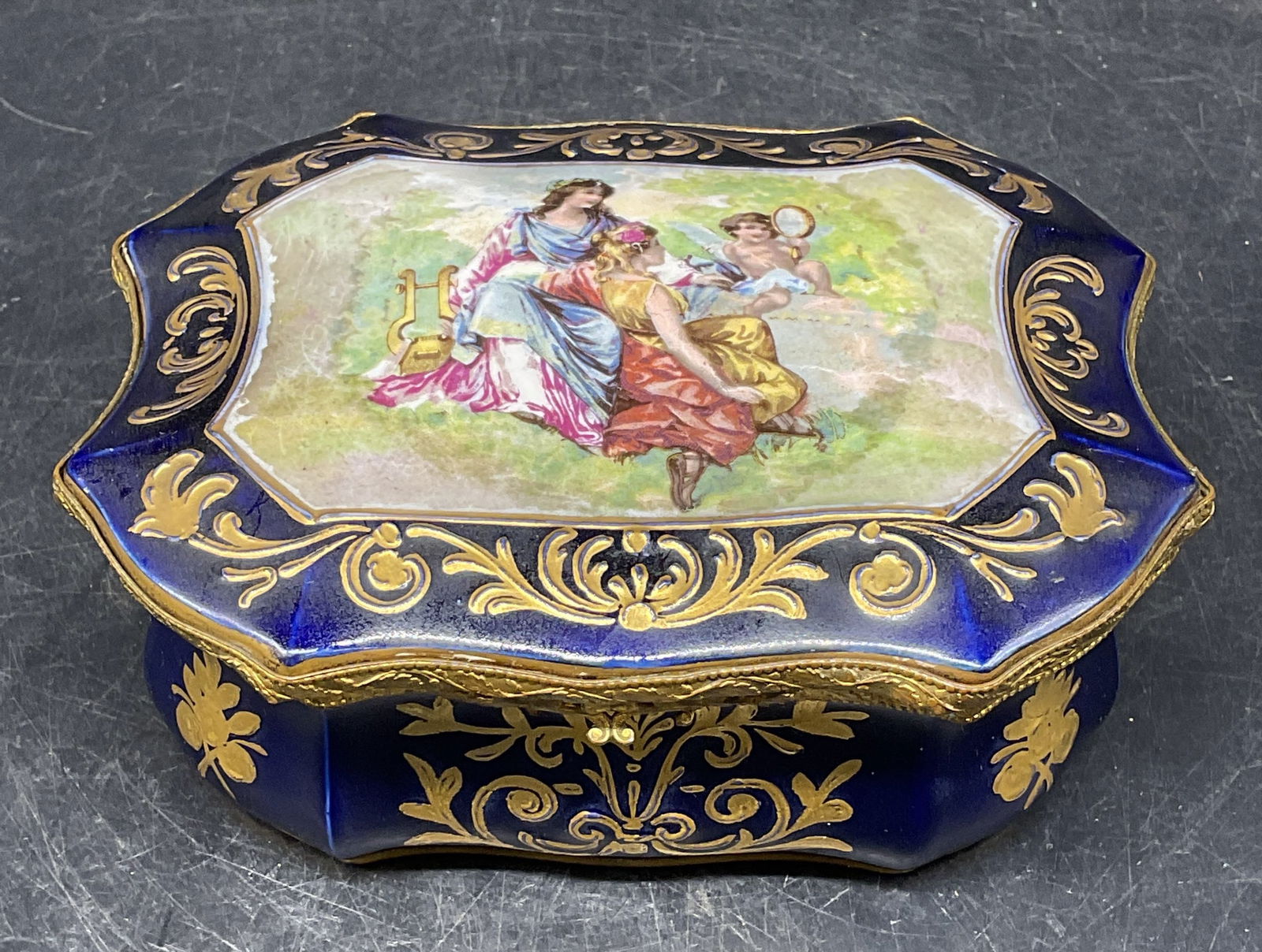 Antique Signed Porcelain Figural Jewelry Box: Antique signed porcelain jewelry box. Hand painted cobalt blue with gilt decoration. Figural scene on lid, floral design on interior. Signed with blue underglaze, crown and monogram mark. Measures app
