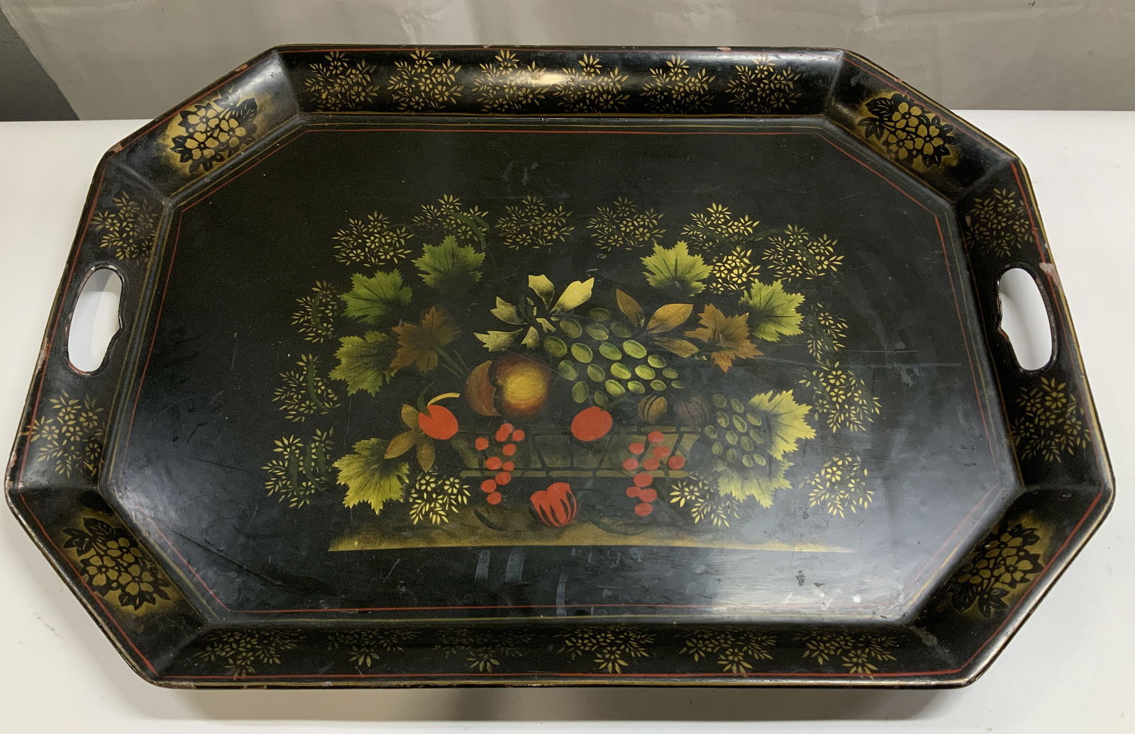 Vtg Hand Painted Fruit Toleware Srving Tray 24in: Large vintage toleware serving tray features a black finish & hand painted fruit motifs in center. Gilt accents. Octagonal shape with handles. Surface wear consistent to age, use & exposure. Measureme