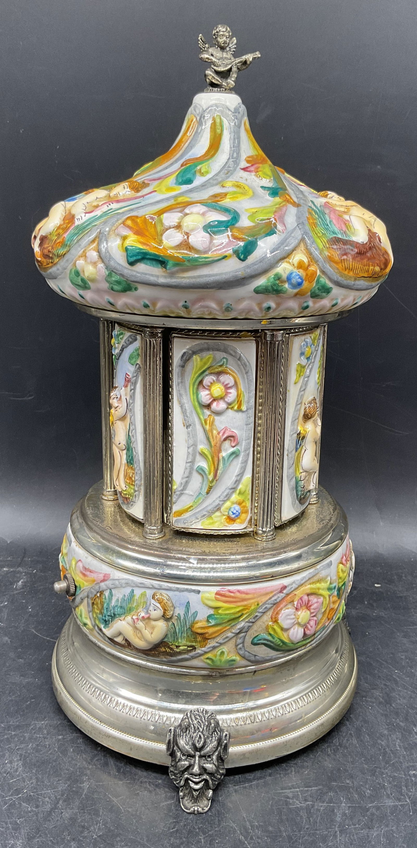 Reuge Enamel Music Box Lipstick Carousel, Italy: Vintage signed Reuge lipstick or cigarette music box carousel. Swiss musical movement. Made in Italy. Capodimonte style porcelain panel decoration. Ornate scroll and cherub design. Figural footed