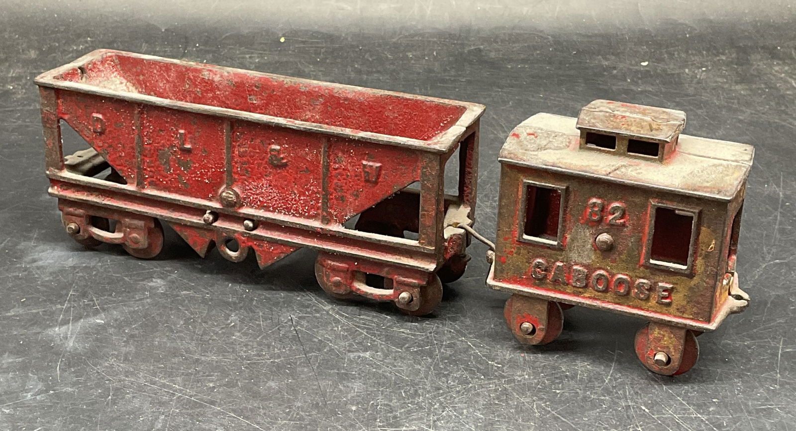 Antique Iron Coal Car & Caboose Toy Train: Antique red iron DL & W coal car and caboose car numbered 82. Coal car measures approx. 6.25 x 1.75 x 2.75 inches. Caboose measures approx. 3 x 1.75 x 3.25 inches. Wear including patina, scratching, l
