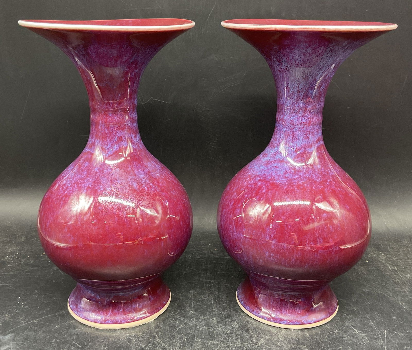 Pair Chinese Porcelain Flambe Bottle Vases: Pair of Chinese porcelain bottle vases. Flambe glaze in red/purple. Round bulb shaped with flared rims. Measures approx. 5.25 x 9.75 inches. Some scratching. Chinese vase, porcelain vase, purple vase,