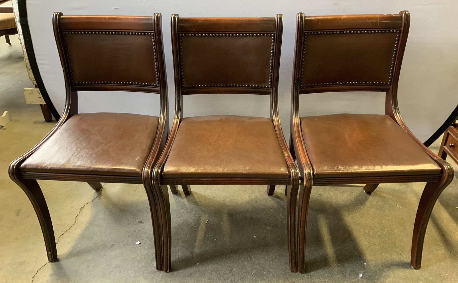 Lot 3 English Regency Style Wood & Leather Chairs: Lot includes, 3 chairs with a curved back & tapered legs. Seat is leather material & backrest has a nailhead trim. Dark toned. English regency style. No visible signature or markings. Surface