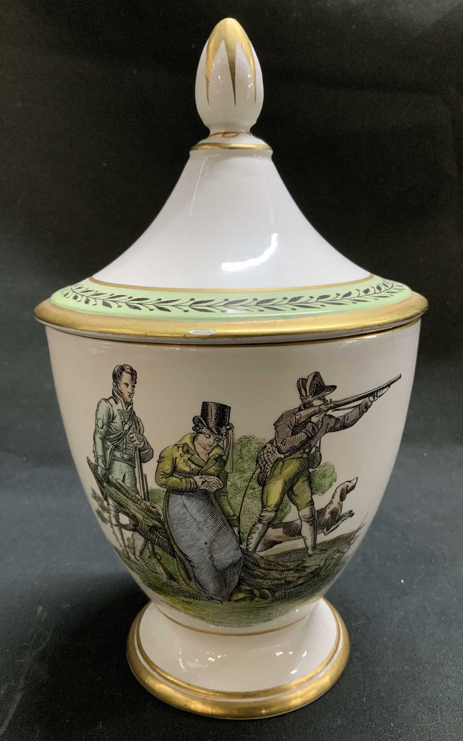 A Mottahedeh Design Illustr Lidded Vessel: A Mottahedeh Design ceramic lidded vessel features an illustrated design of figures wearing 19th century attire. Urn shape. Pointed finial & gilt accents. Signed & marked on underside. Reads, A Mottah
