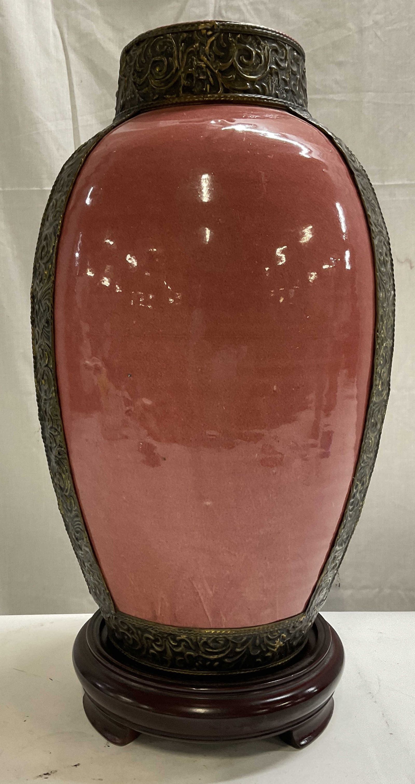 Peach Bloom Glazed Vase with Bronze Toned Overlays: Peach Bloom Glazed Ceramic Vase with Bronze Toned Overlays. Asian-Style. Overlays are metal with intricate designs engraved. Sits on wooden stand. Some crazing and wear to metal consistent with exposu