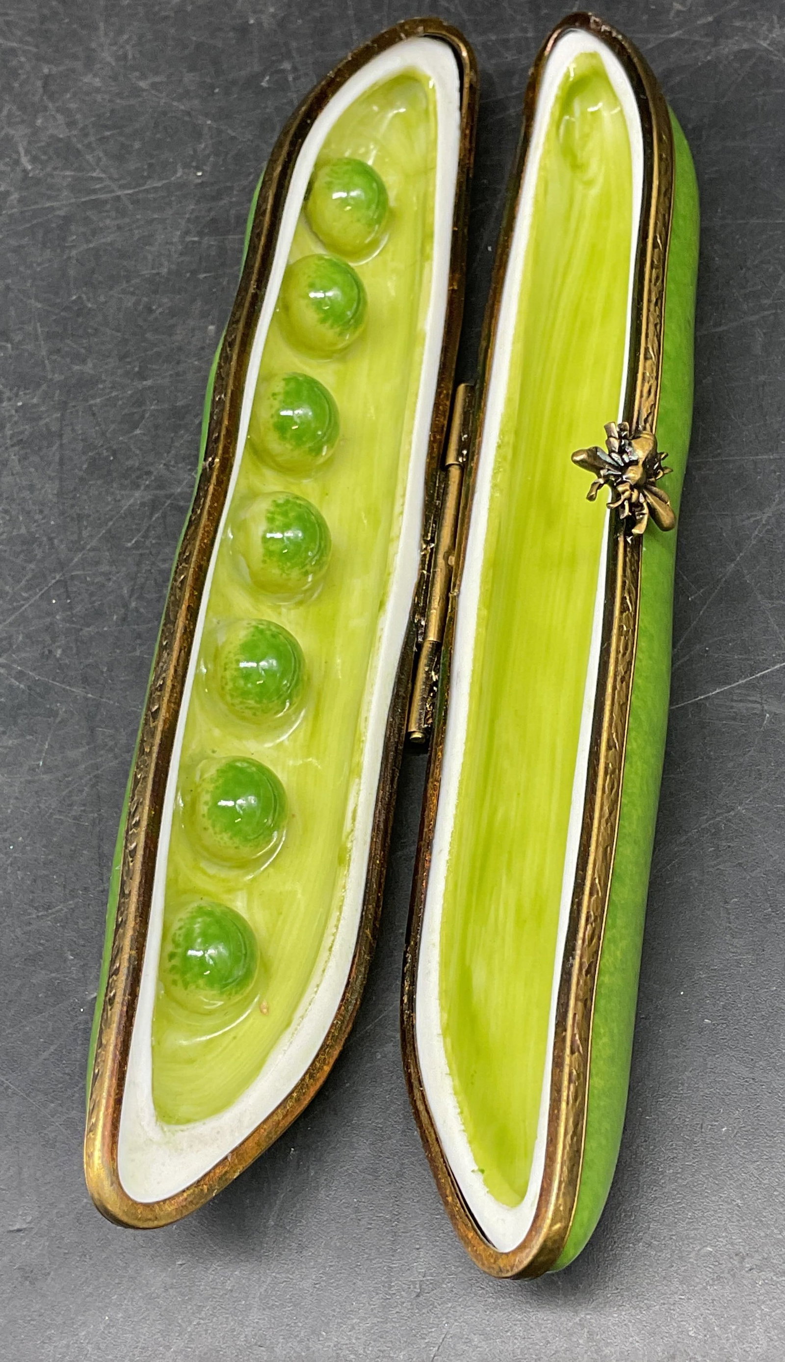 Limoges Porcelain Pea Pod Trinket Box, France: Signed DZ Limoges porcelain trinket box. Pea pod with raised peas on interior. Gold tone bee motif latch and frame. Hand painted. Made in France. Measures approx. 5.25 x 1 x 1 inches. Some scratching.