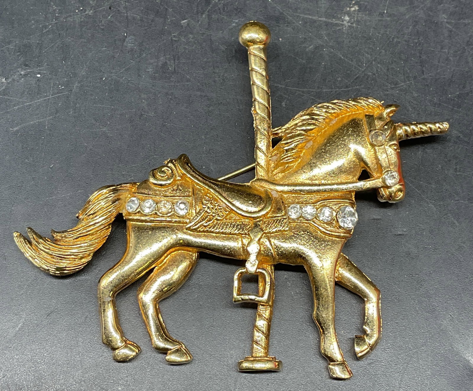 Vintage Gold Tone Carousel Unicorn Brooch: Vintage gold tone carousel unicorn motif brooch with crystal decoration. Measures approx. 2 x 3.25 inches. Some scratching and warping. Jewelry, estate jewelry, costume jewelry, cocktail jewelry, fash