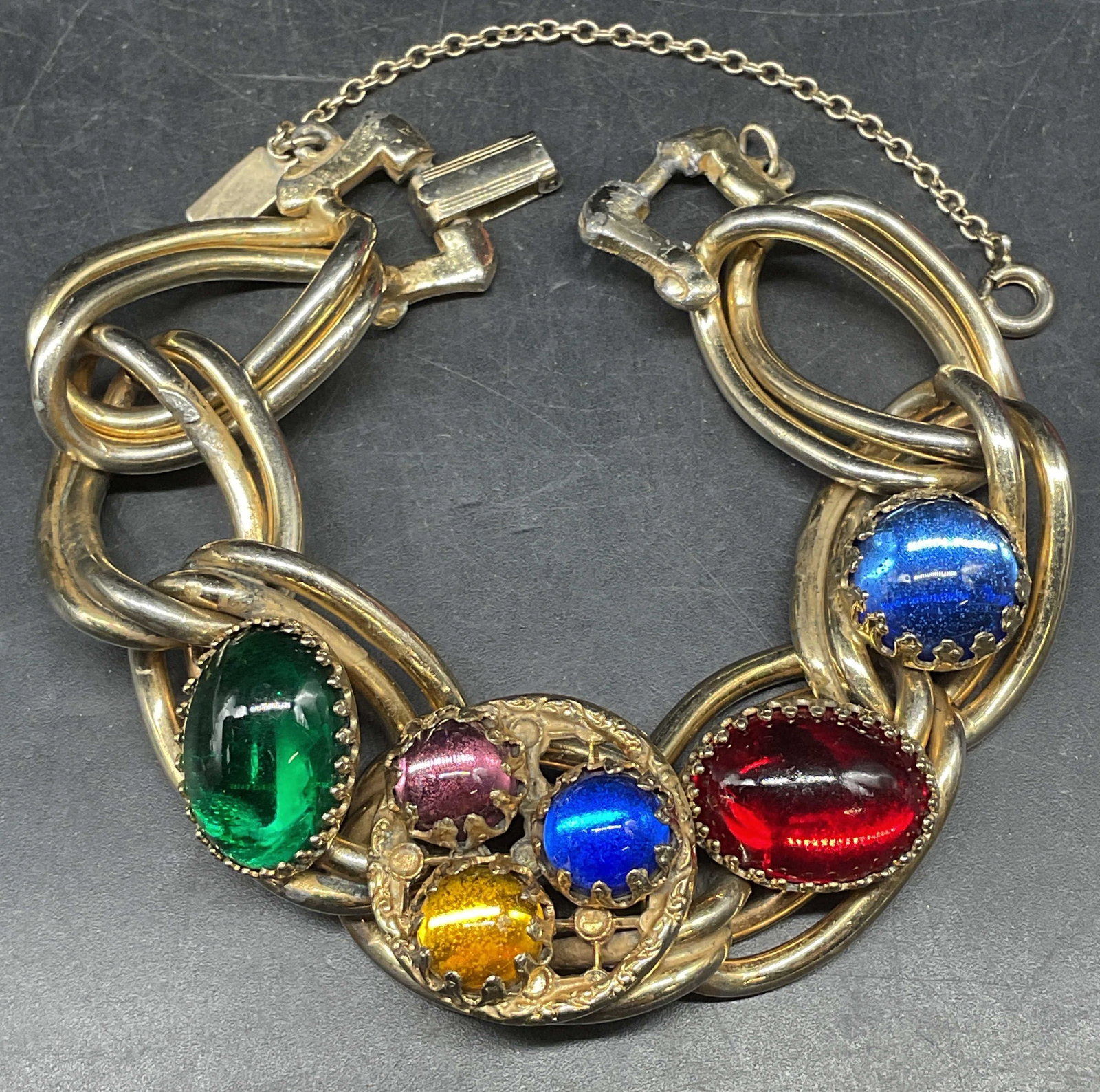 Vintage Reinad Gold Tone Jeweled Bracelet: Vintage signed Reinad New York chunky gold tone bracelet with multicolored faux jewel cabochons. Measures approx. 7 inches long. Clasp needs repair. Some scratching. Includes a box. Jewelry,